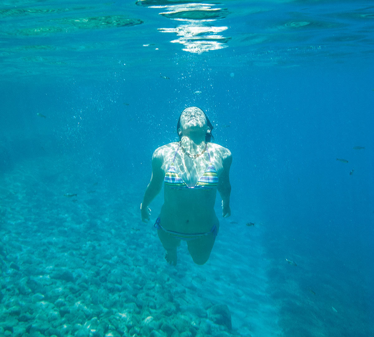 A person swims toward the surface in crystal-clear blue water