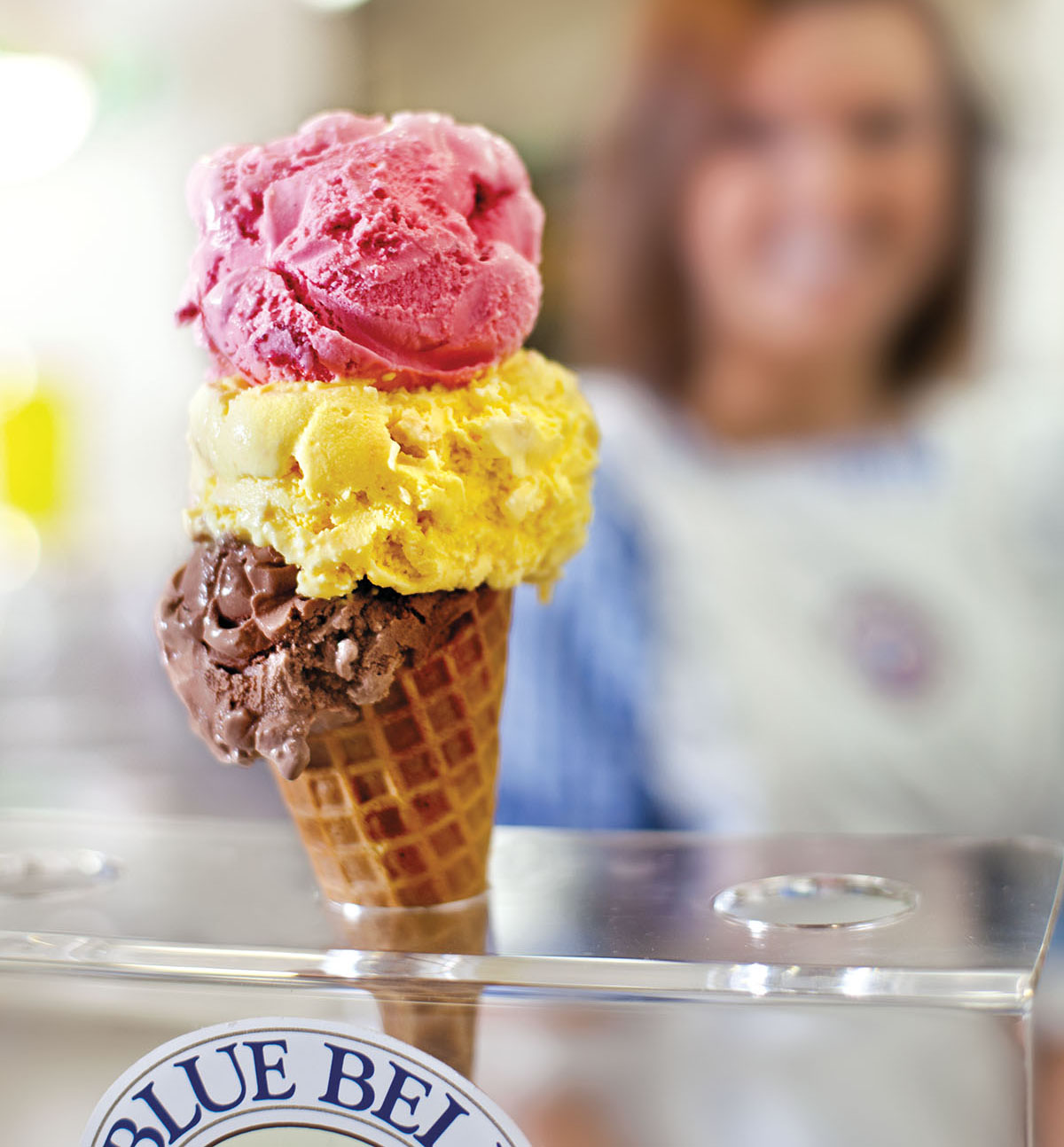A waffle cone of ice cream filled with bright pink, yellow, and brown scoops