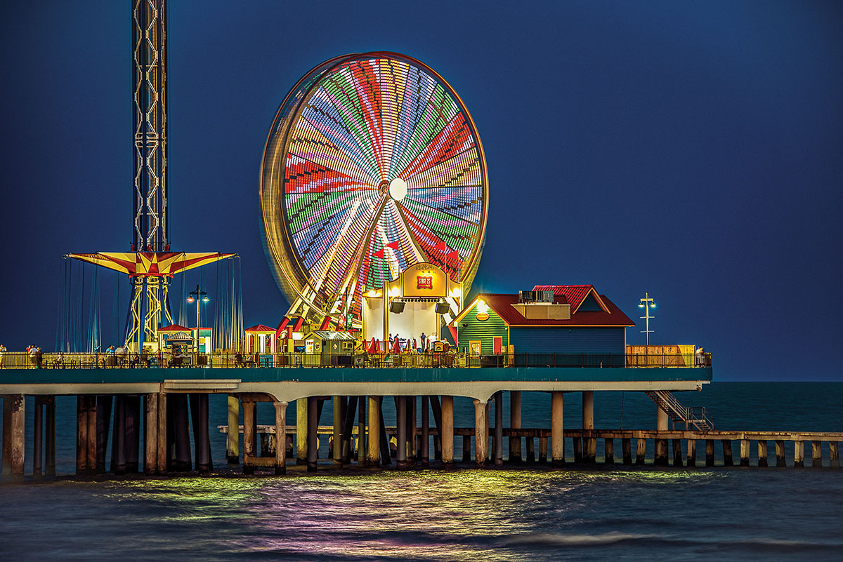 A colorful Ferris wheel on a long wooden pier over blue water