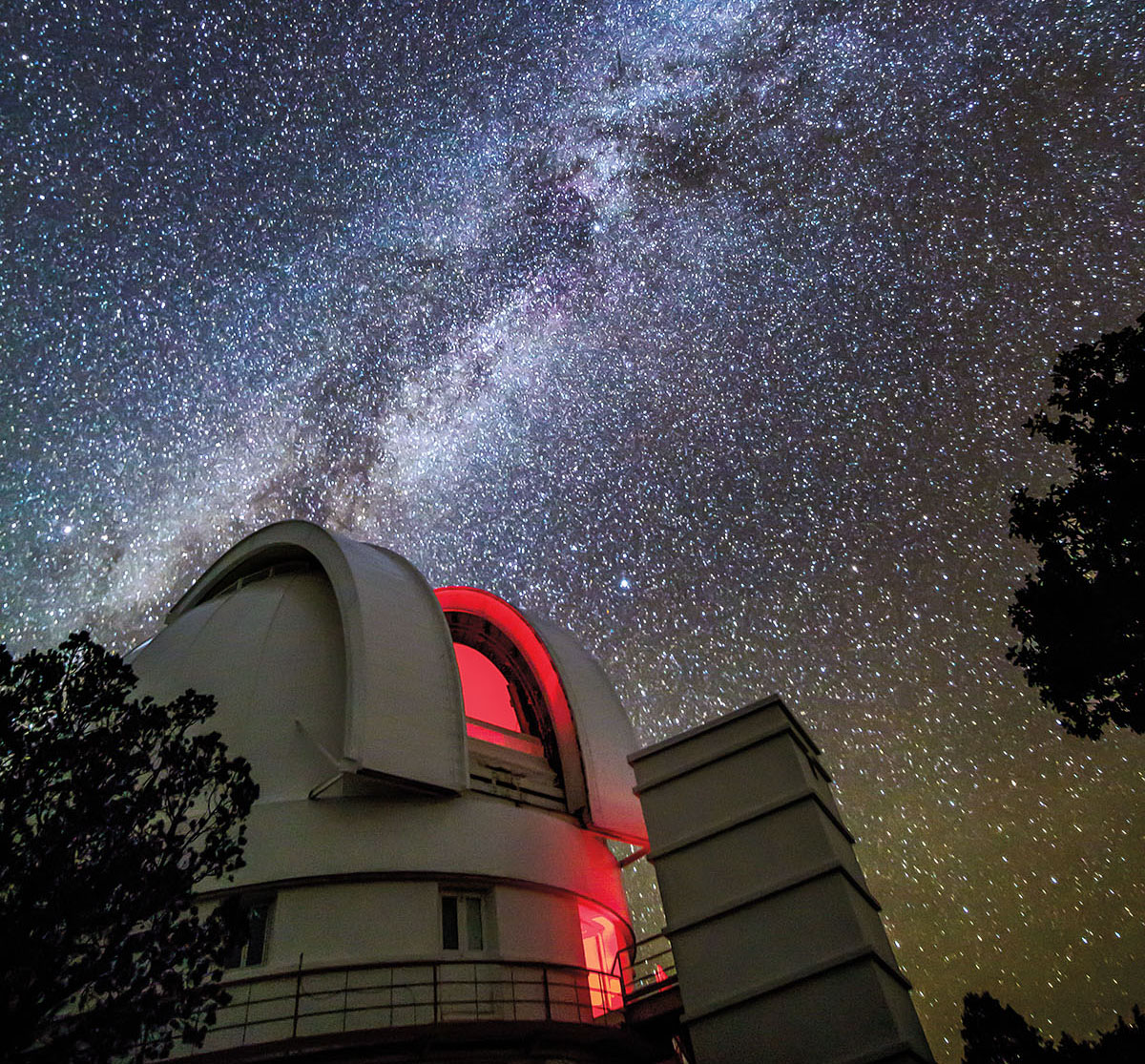 A nighttime photograph of a large white telescope and sky full of stars