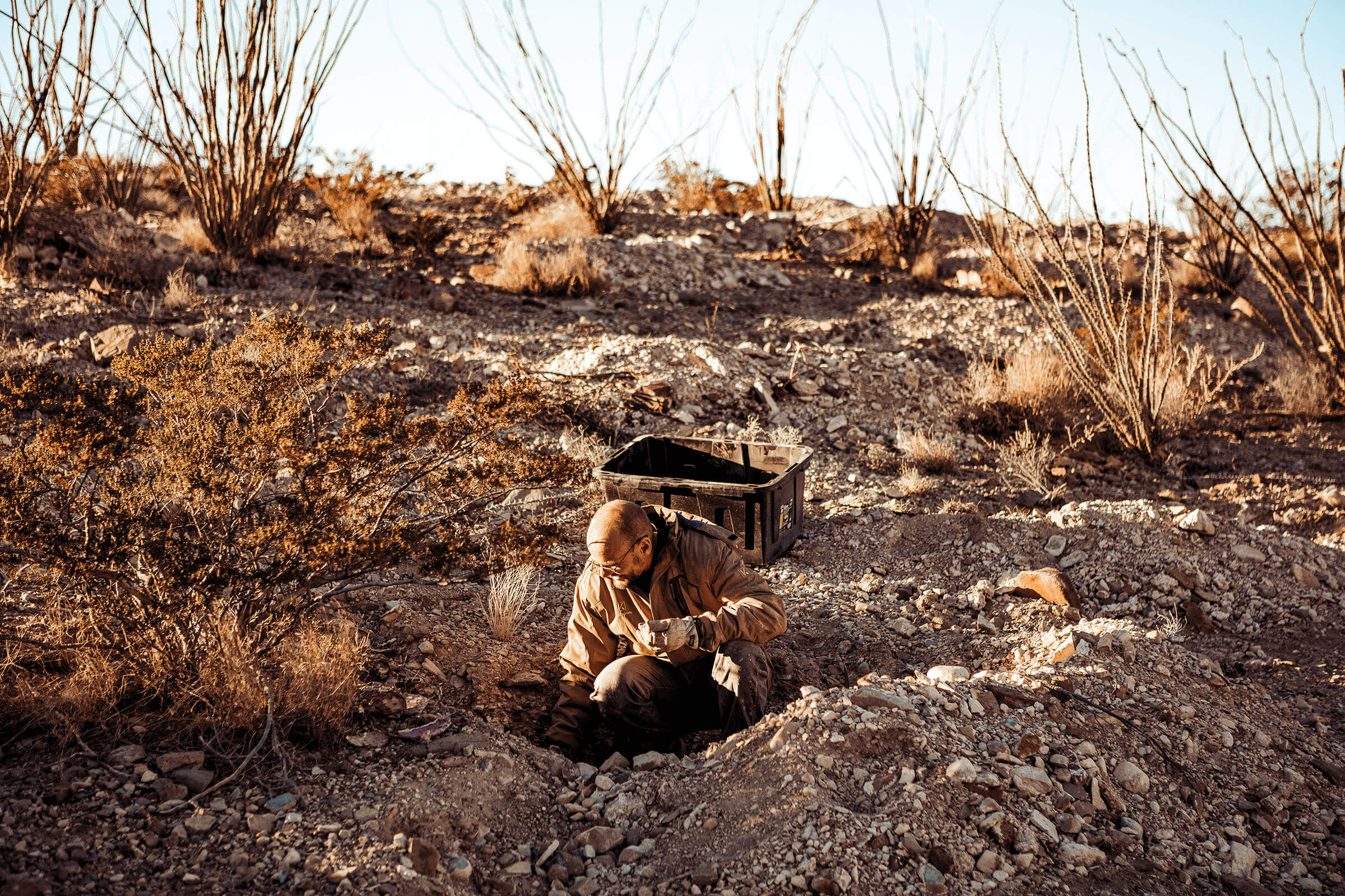 A man digs in a dirt hole in a desert landscape