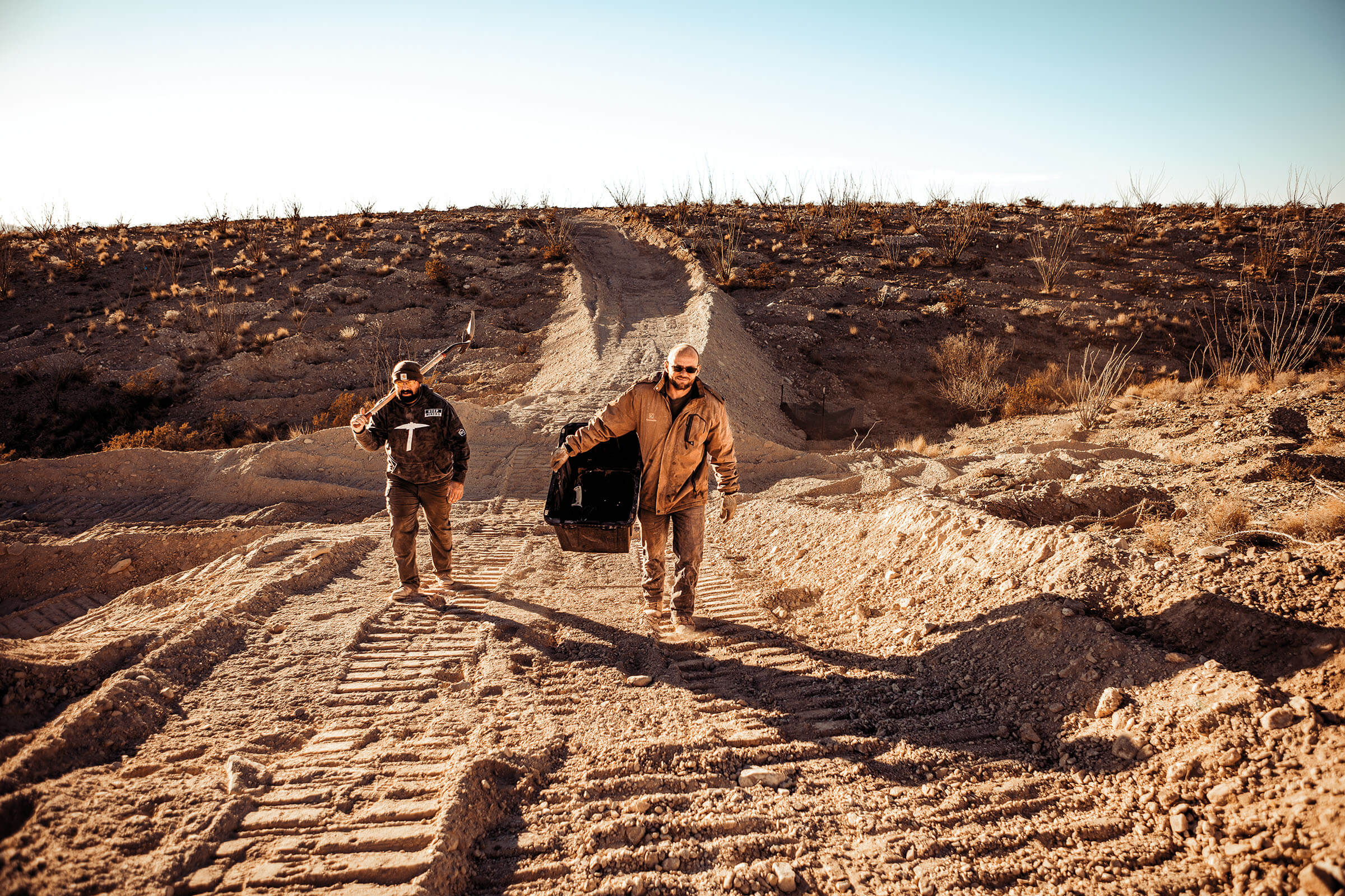 Two men walk down a dirt road under blue sky