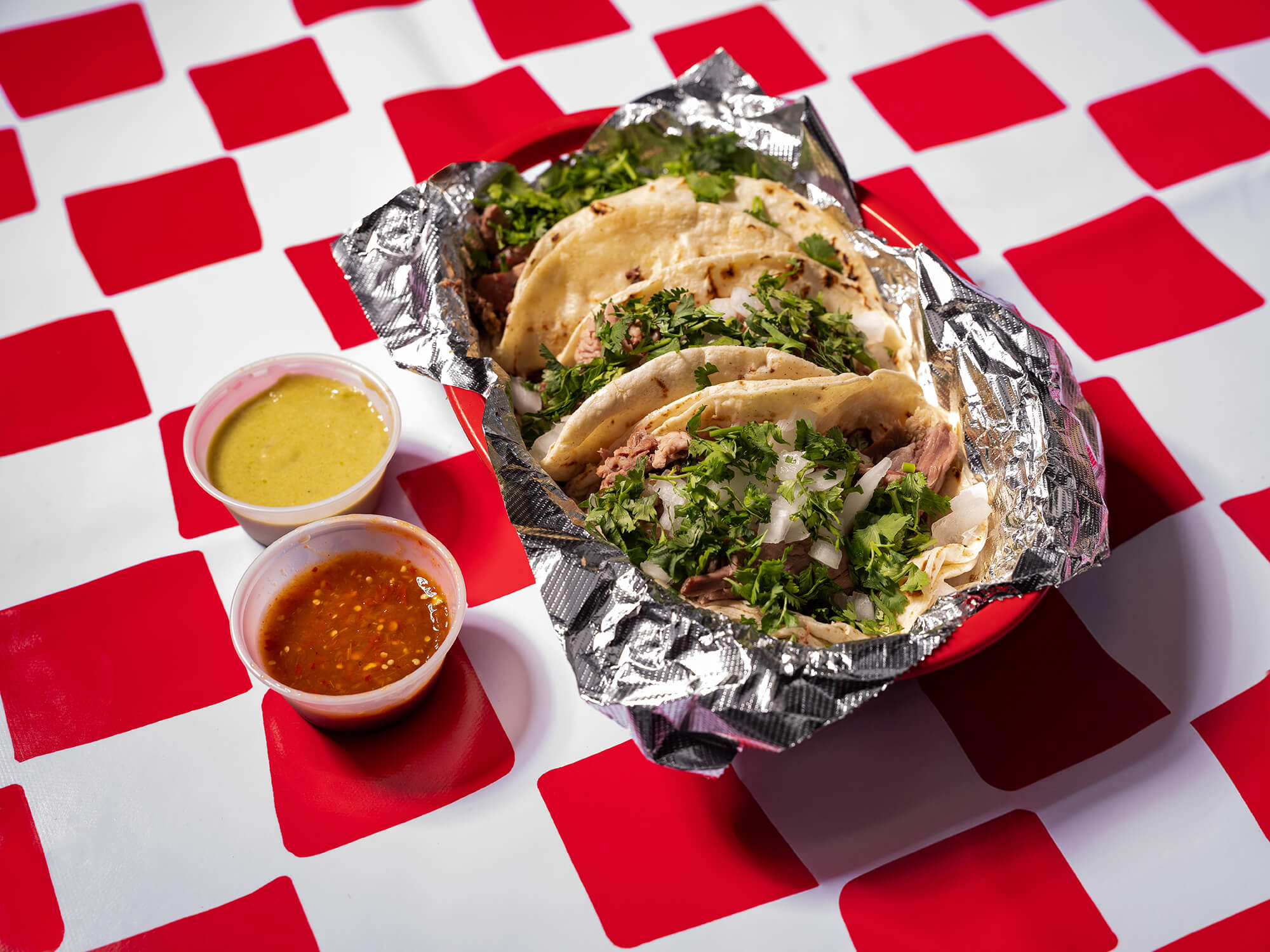 A basket of barbacoa tacos topped with onion and cilantro on a red-and-white checkered tablecloth