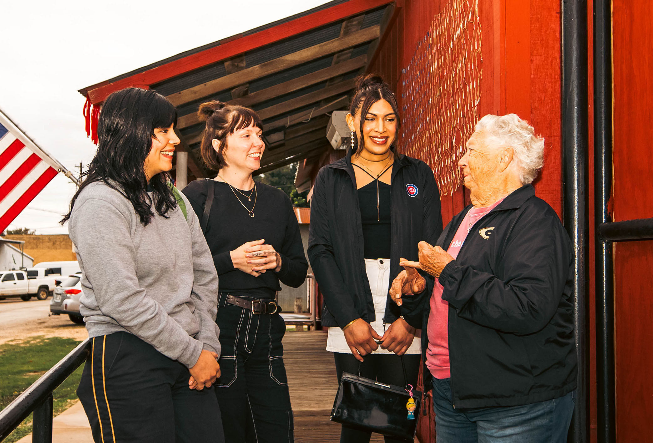 A group of women stand talking outside of a red building 