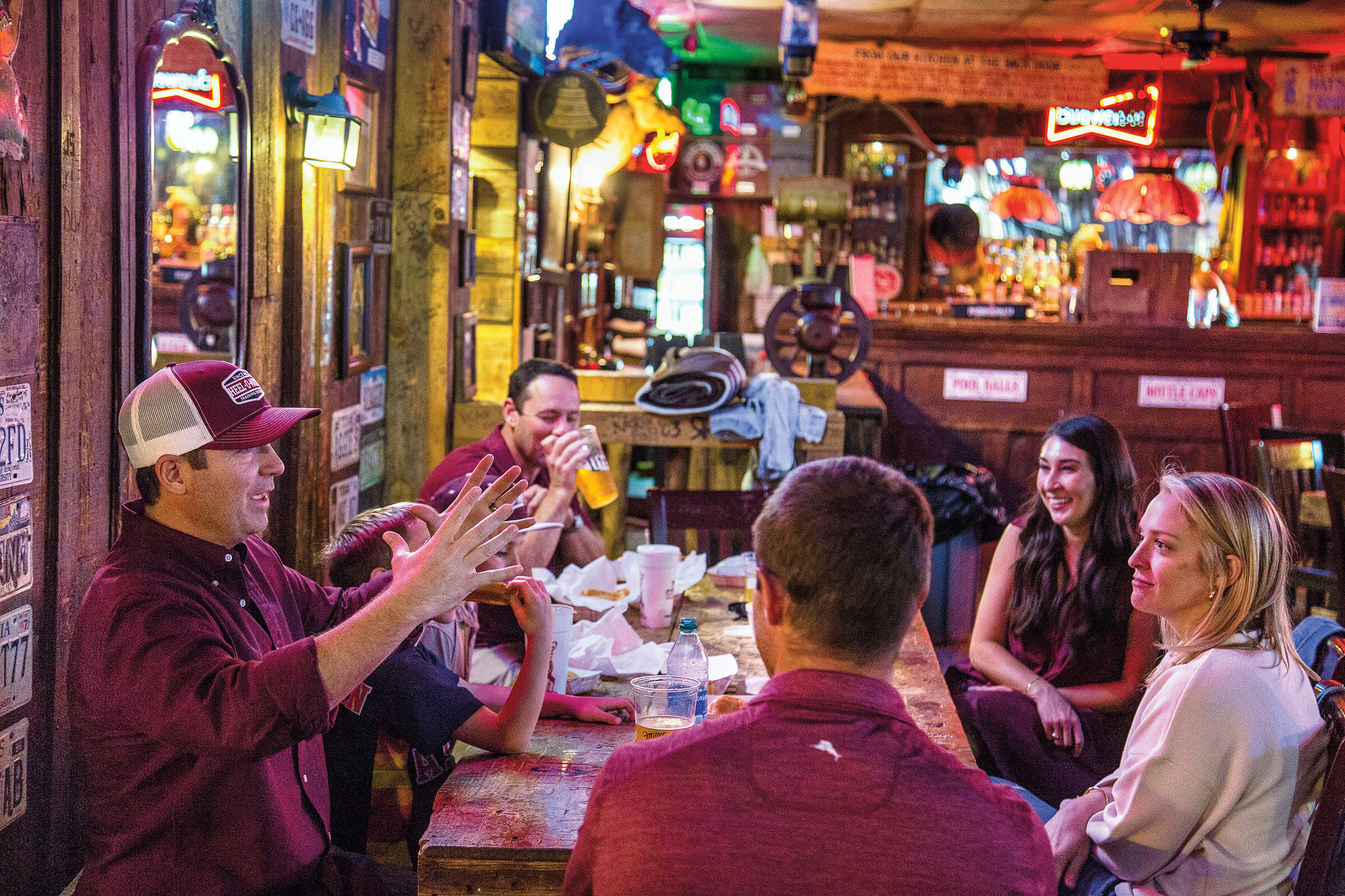 A group of people wearing Aggie attire talk at a bar