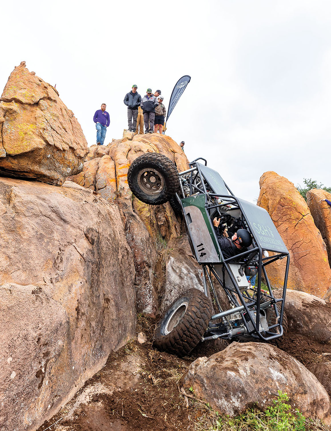 A person driving a green and black 4x4 vehicle attempts to scale a tan rock
