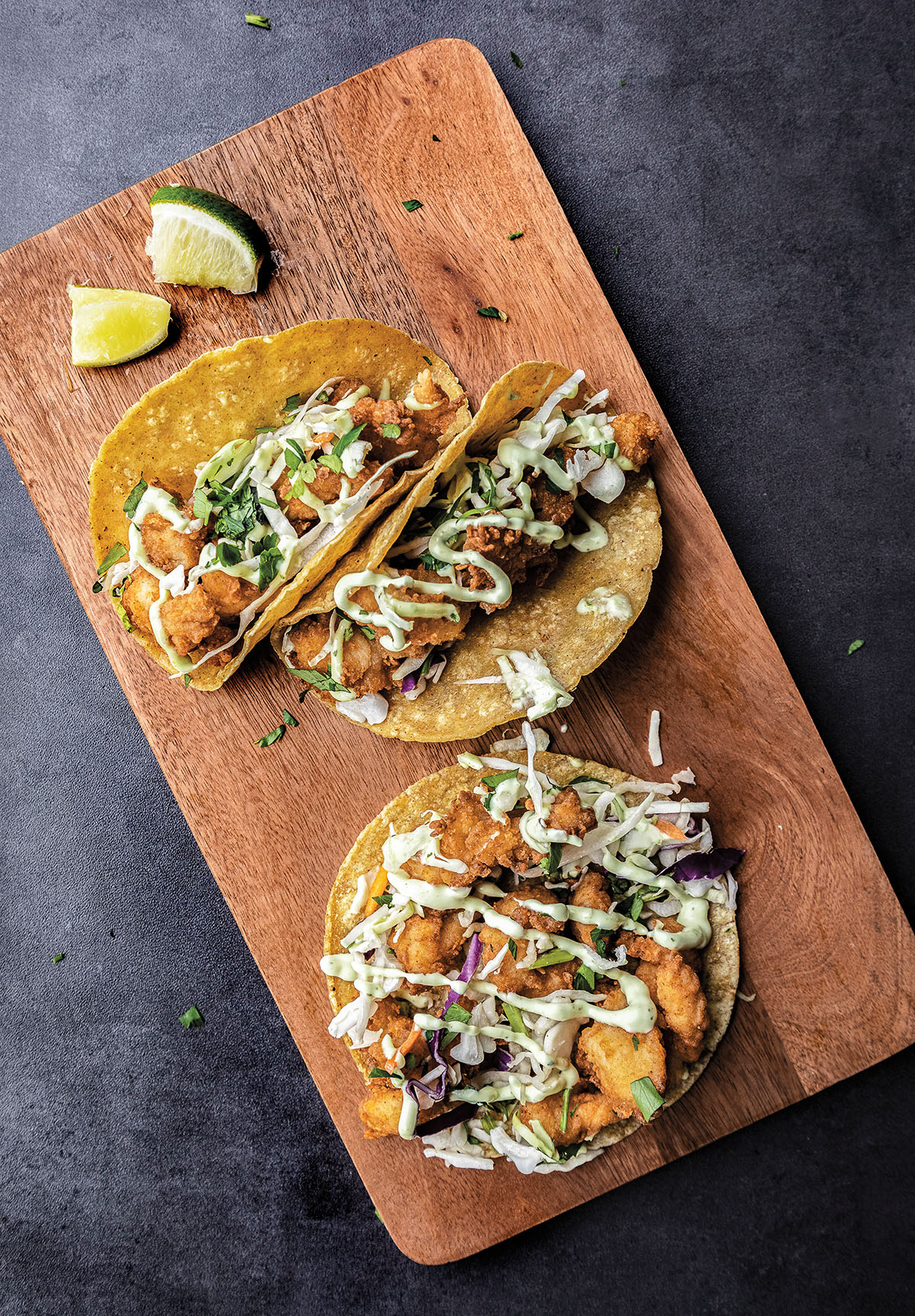 An overhead view of tacos on corn tortillas served on a wooden platter with limes