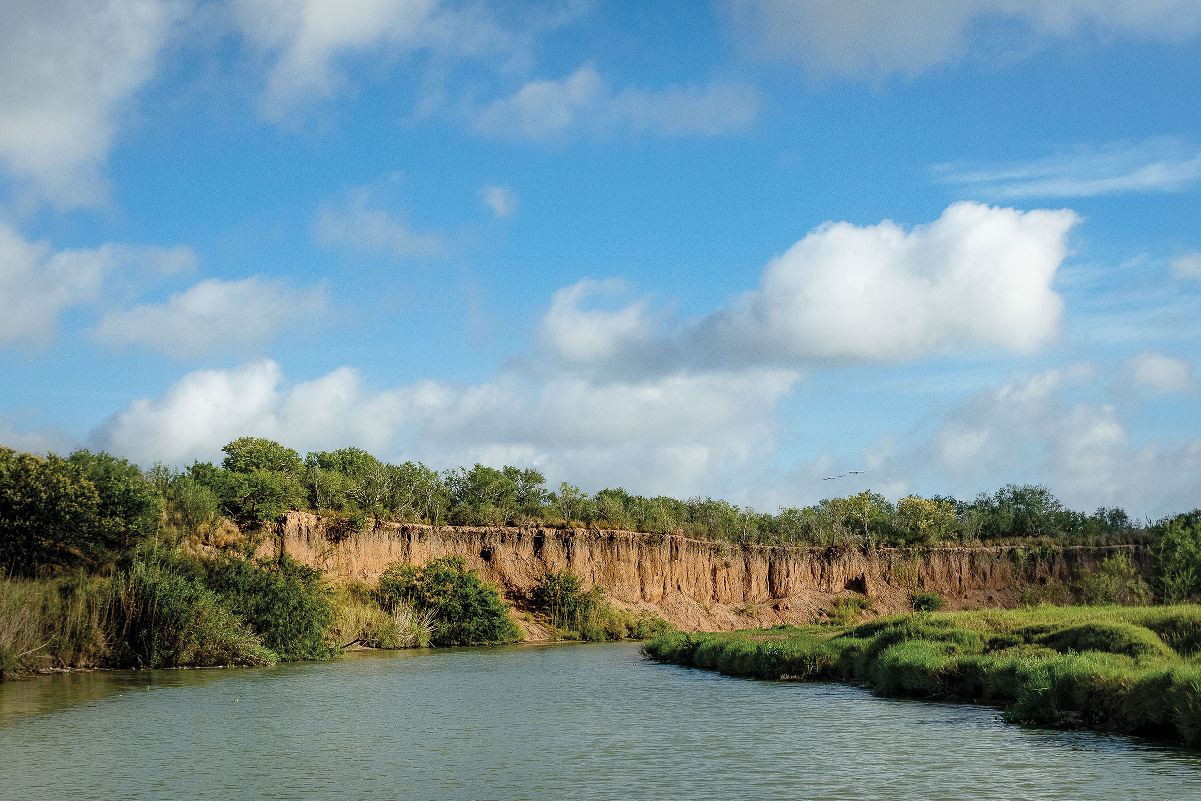 A rock outcropping with green trees above a wide blue river under a clear blue-sky day