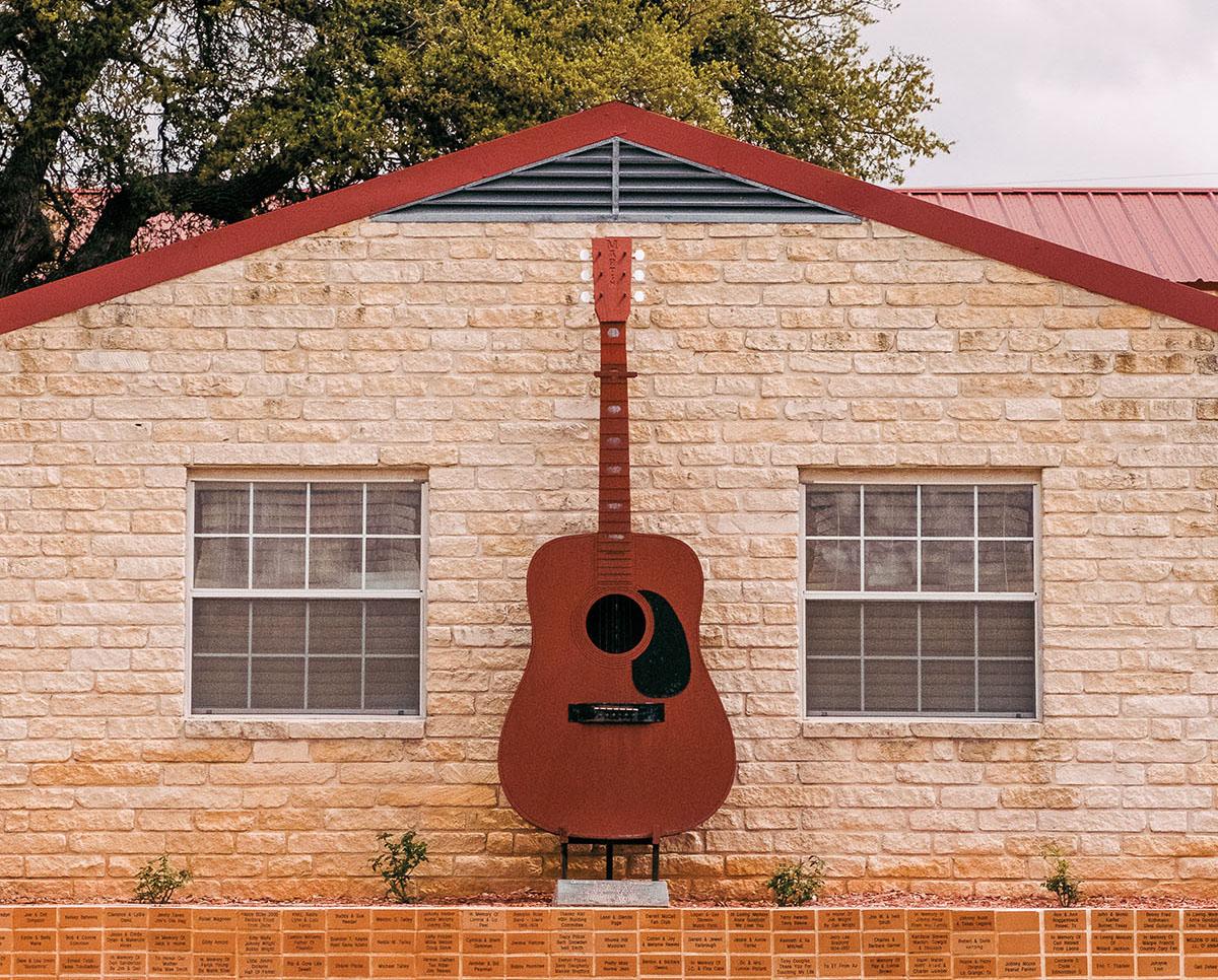 A guitar on the exterior of a light limestone building with a red roof