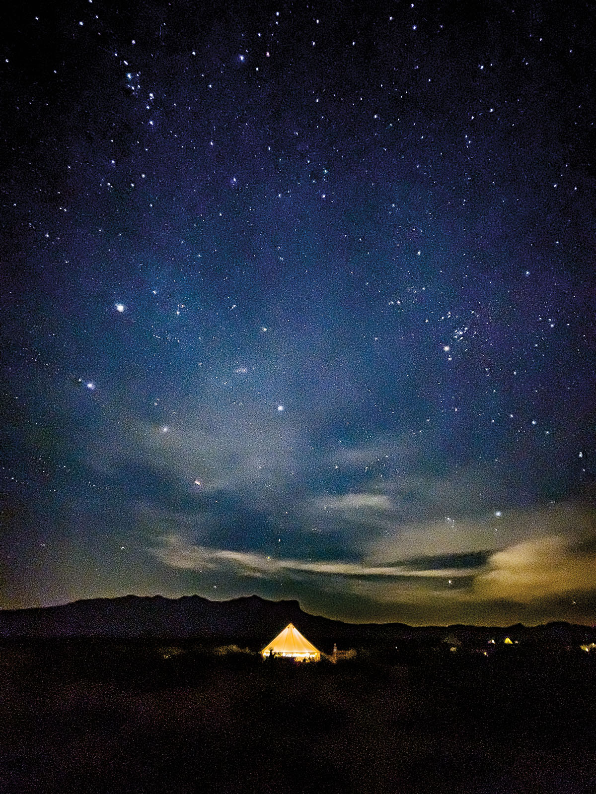 A lit-up yellow tent under a large, deep-blue starry night sky