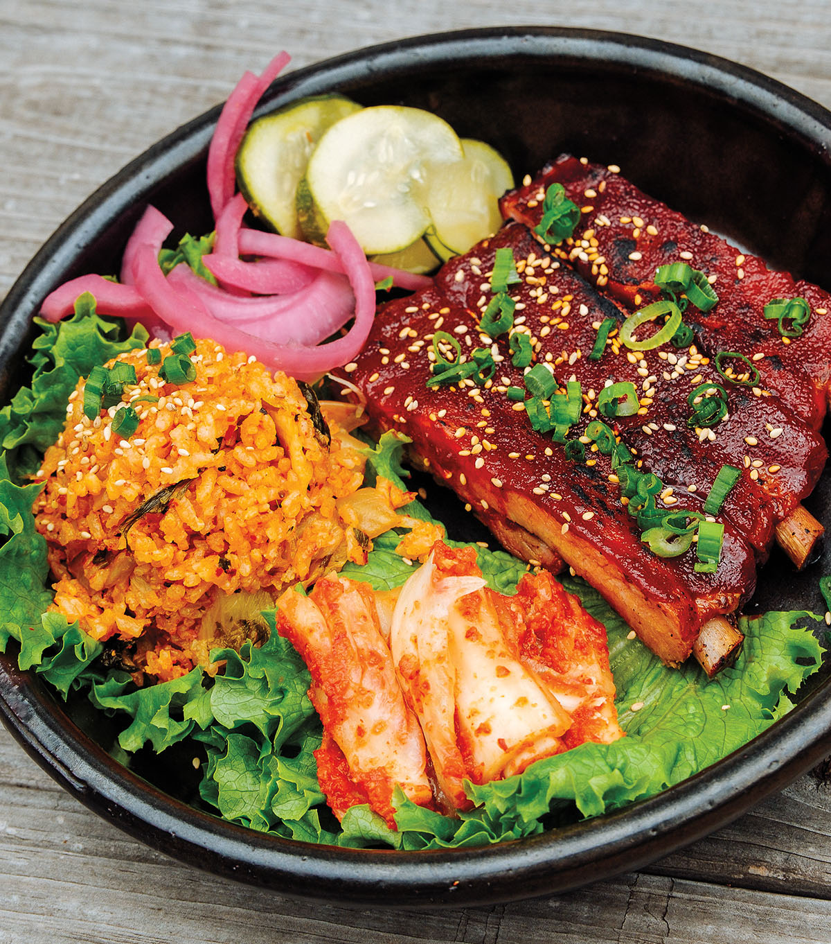 A bowl of vegetables, kimchi, golden rice, pickled vegetables, and pork ribs
