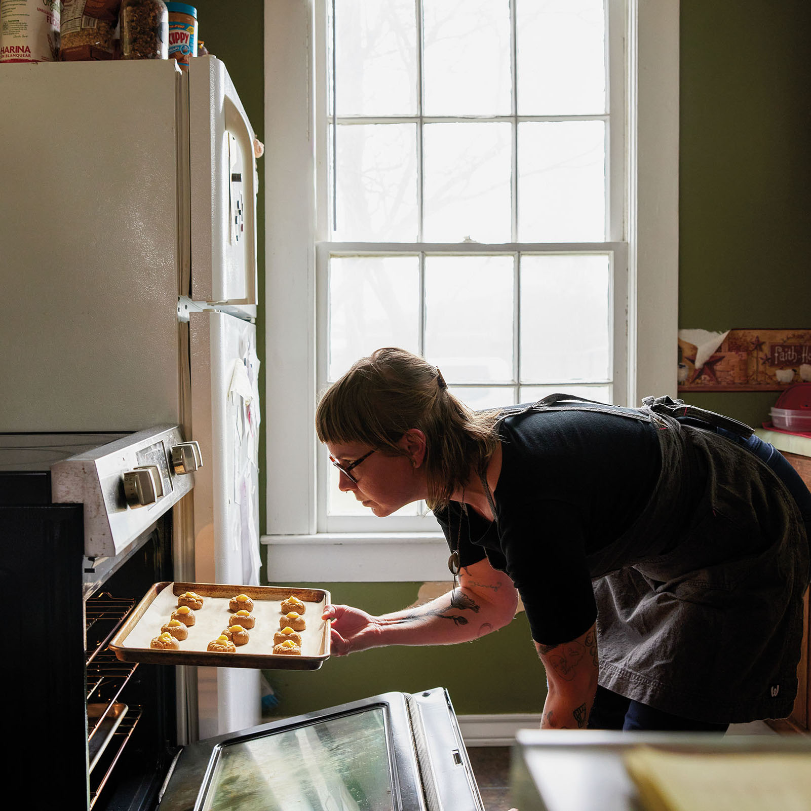 A person places baked goods into an oven in front of a large window