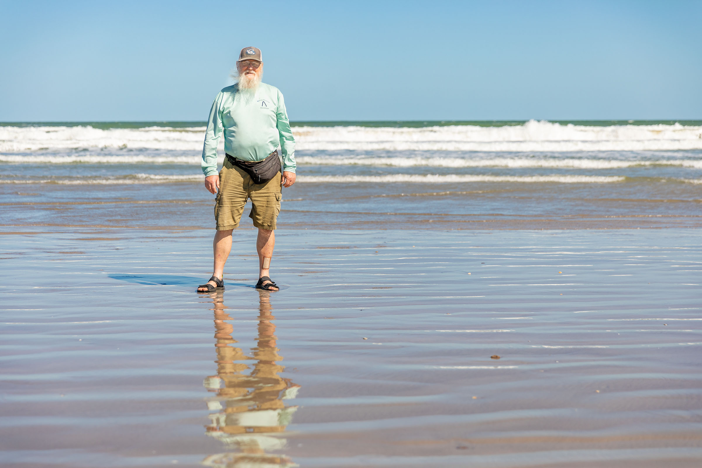 A man in an aqua blue shirt stands on the seashore
