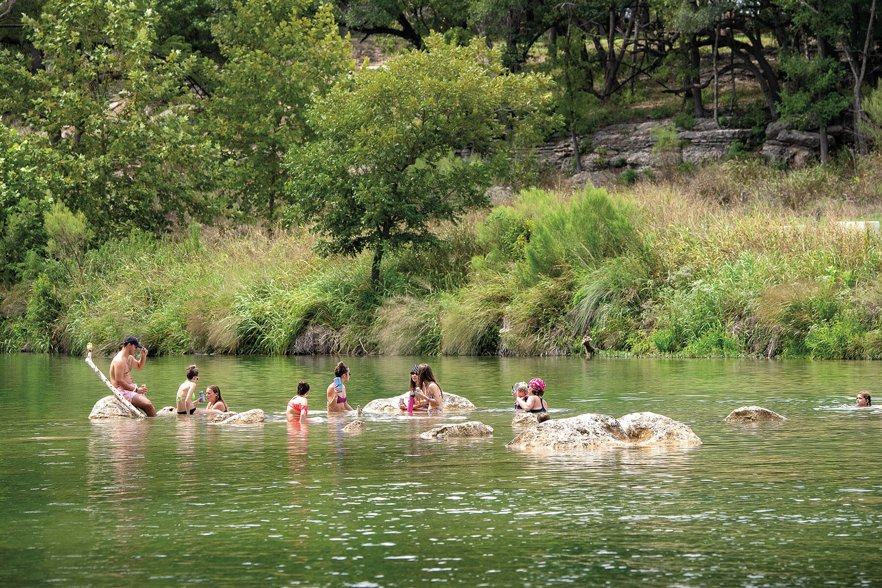 A group of people swim around rocks in a clear green river