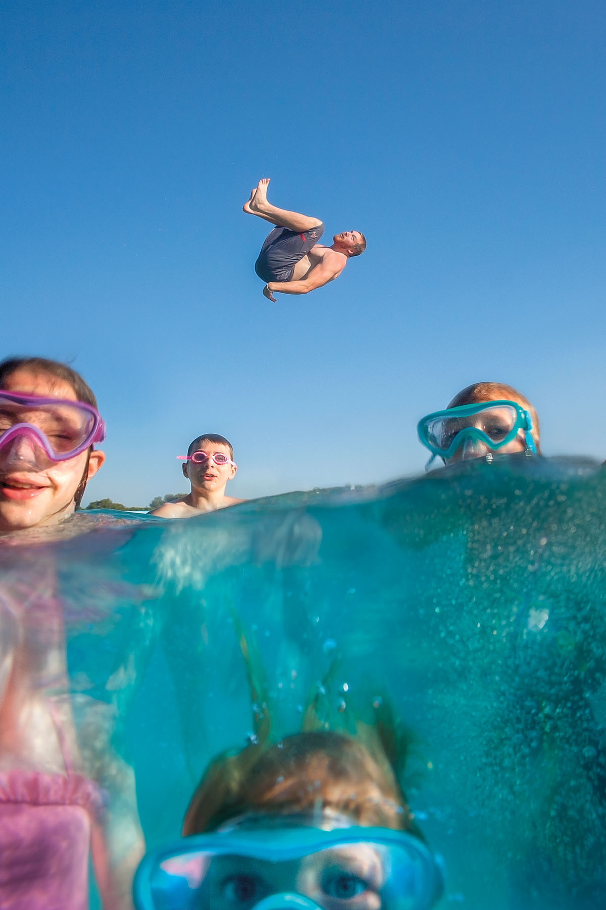 A person does a backflip into crystal blue water while a group of people swim and snorkel