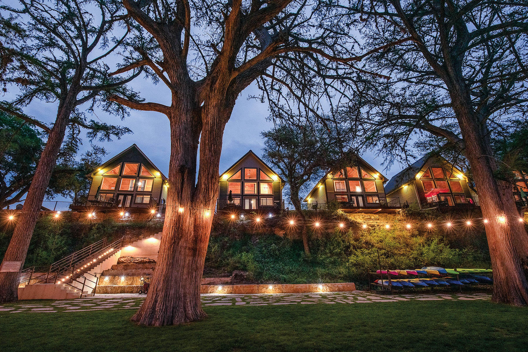 A large lodge with golden string lights under tall trees