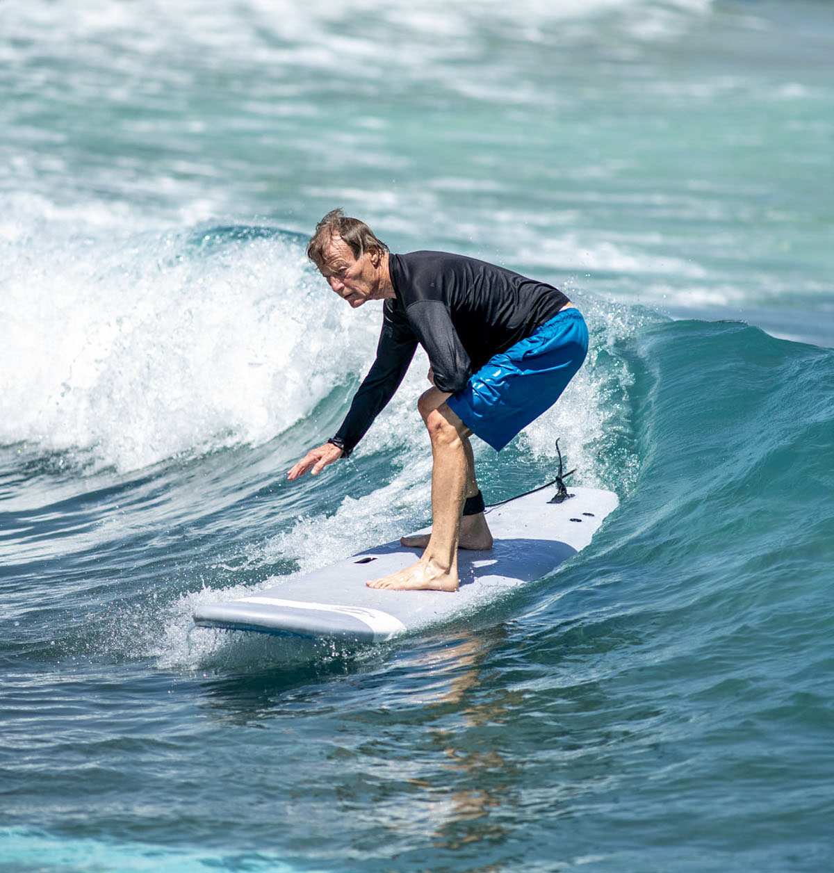 A man in swimwear rides a surfboard on a large blue wave