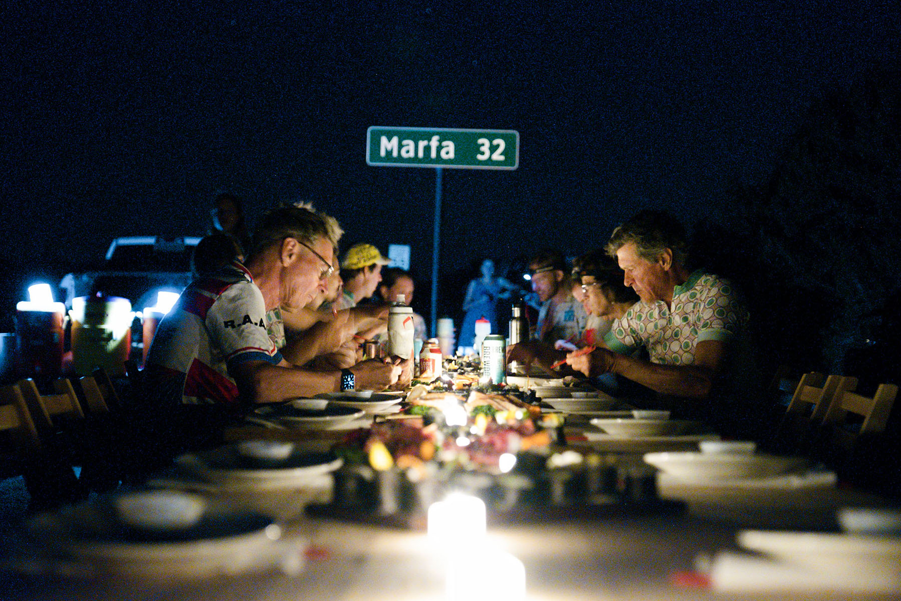 A group of people eat sushi at dark at a table with lights down the center and a sign reading 