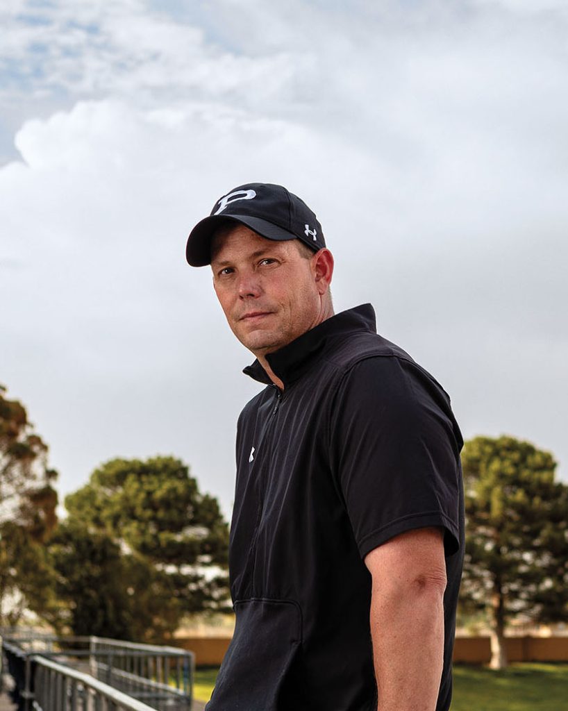 A man in a black polo shirt and black ball cap looks at the camera
