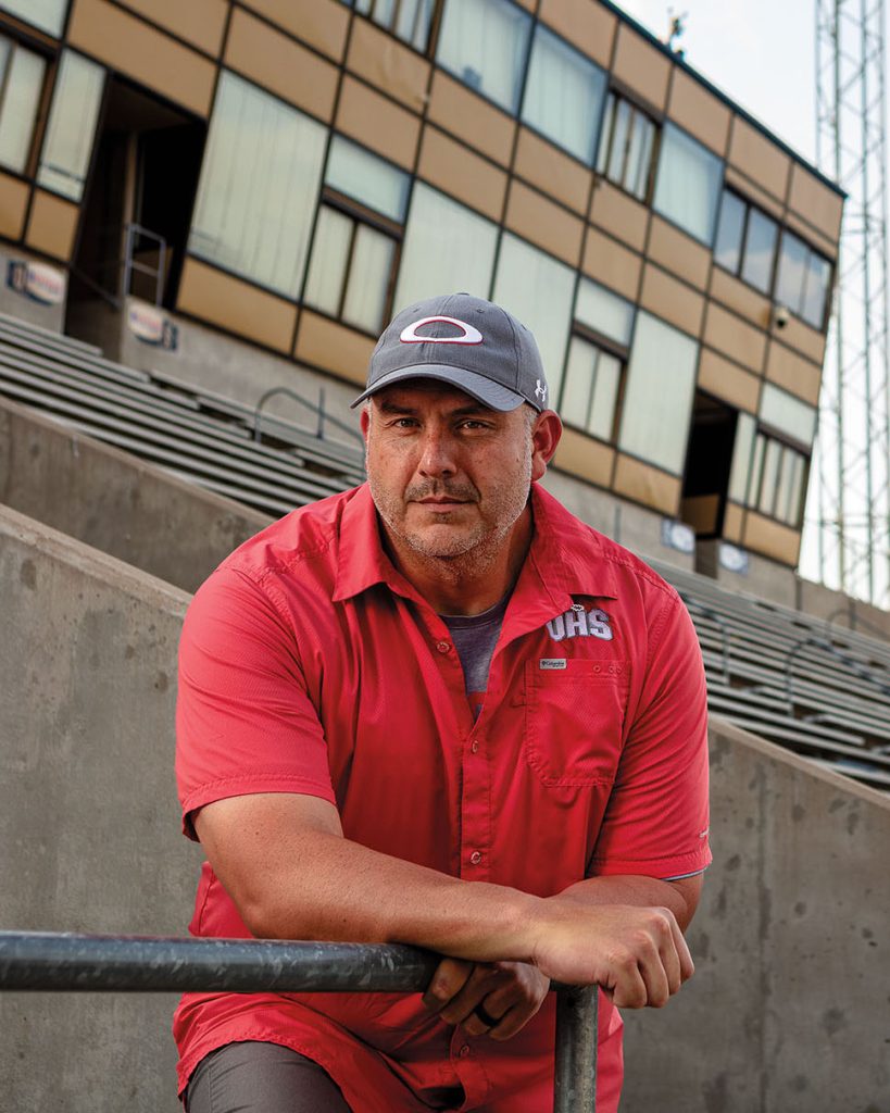 A man in a red shirt and gray baseball cap looks at the camera