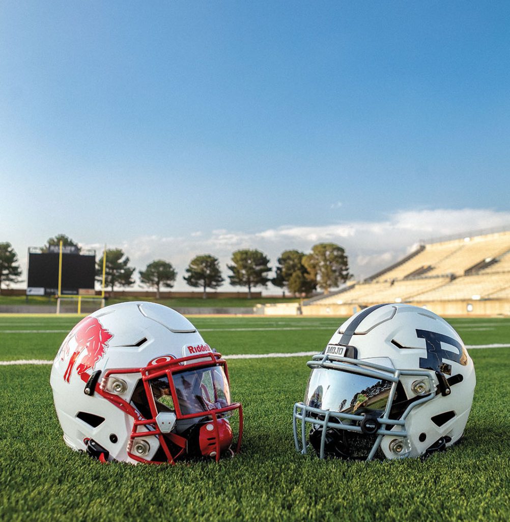 Two helmets sit on a bright green turf football field under blue sky