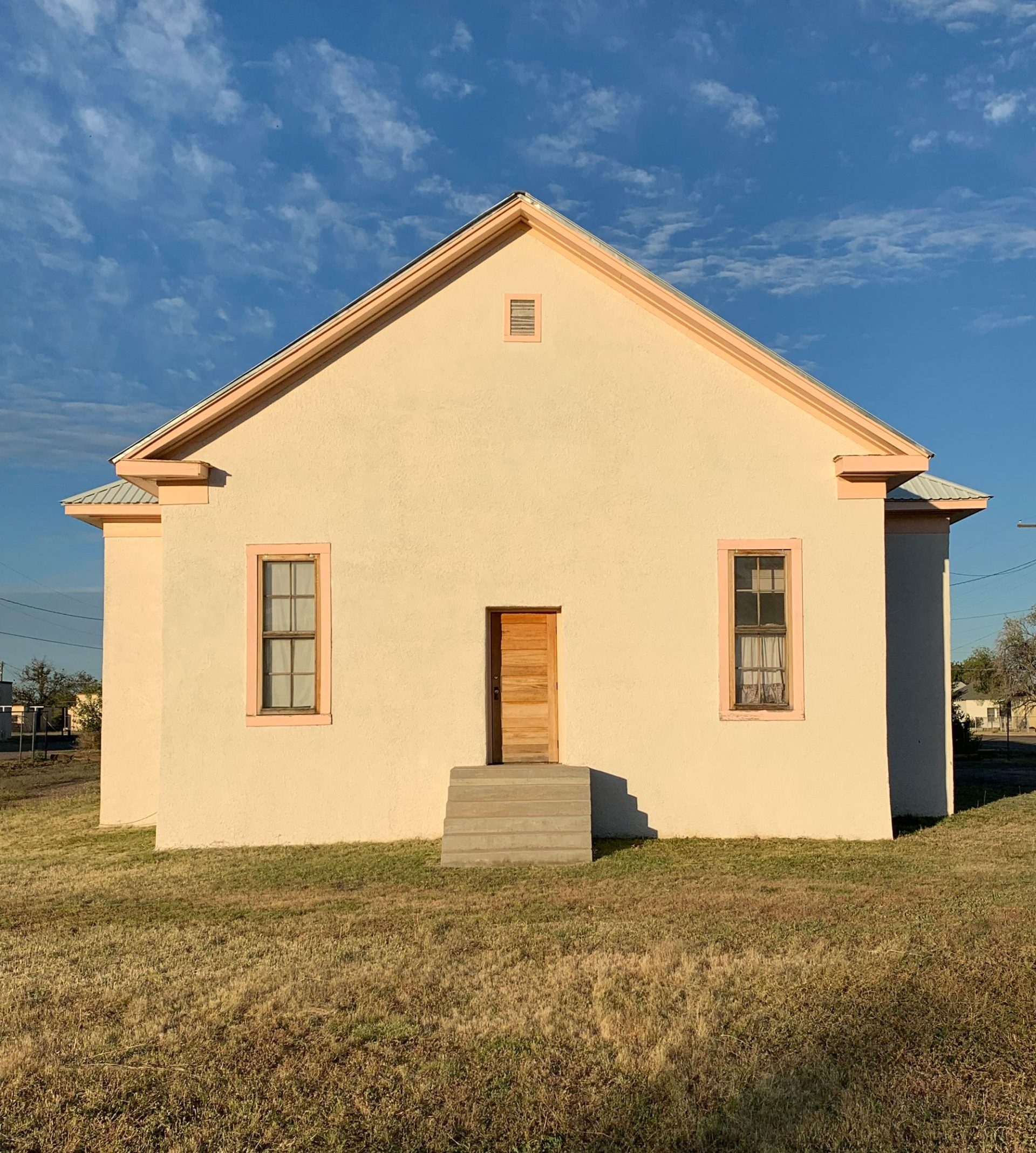 A white house with a wooden door and pink window frames