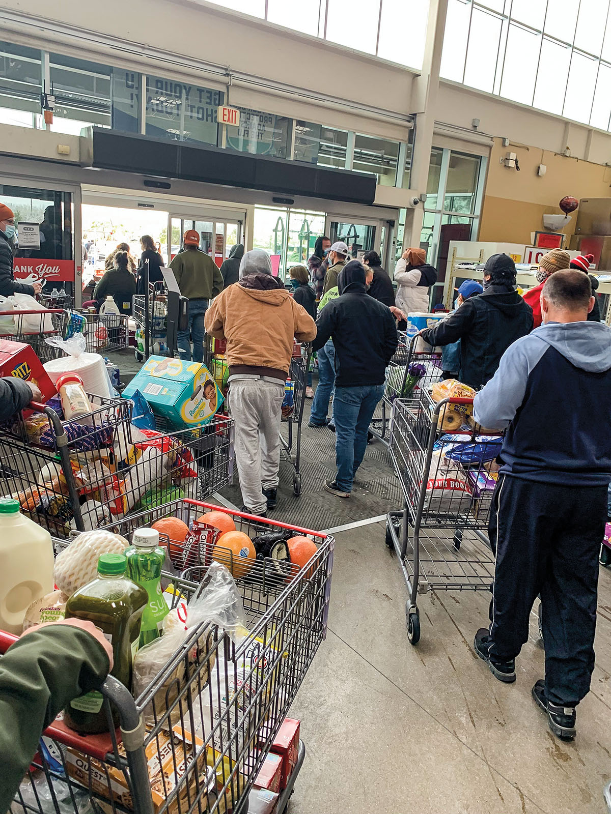 A group of people walk toward the exit of an H-E-B with shopping carts