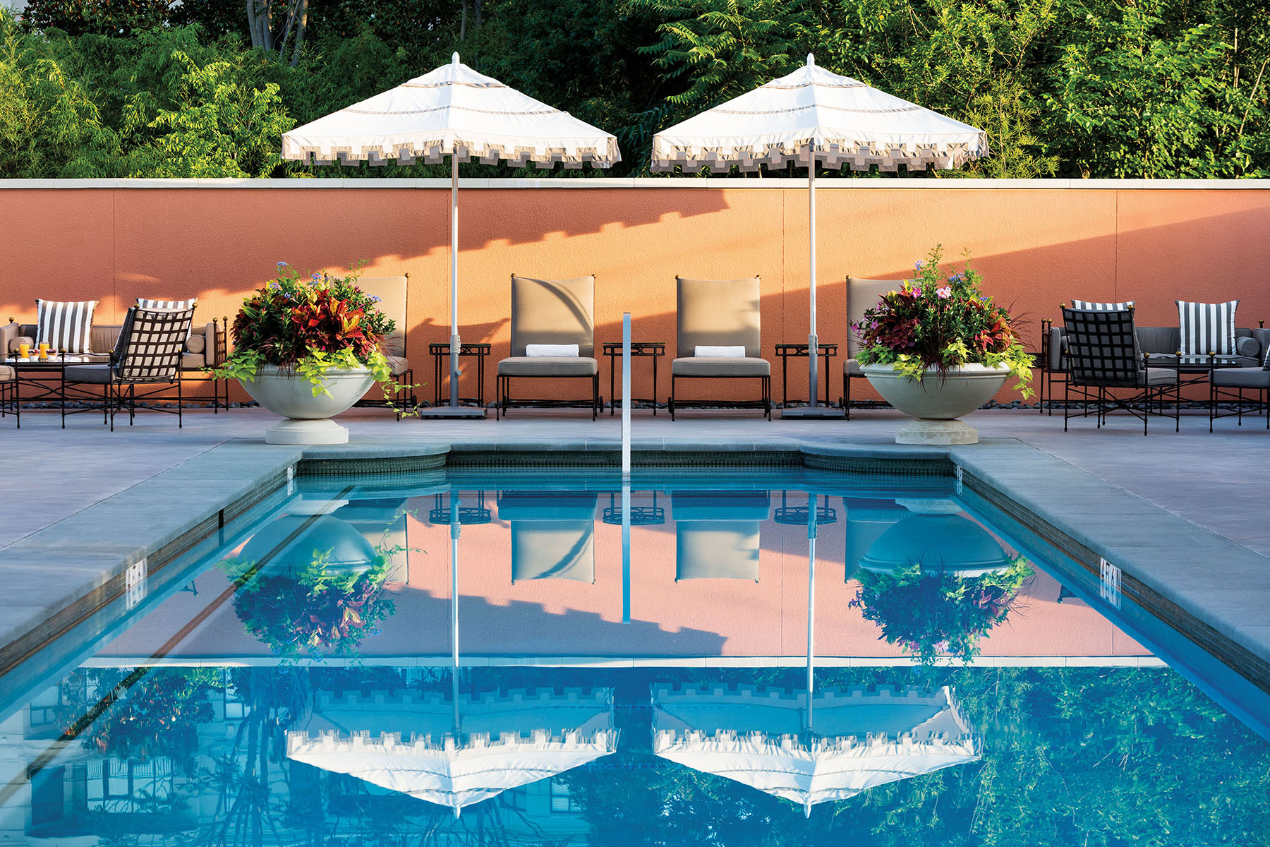 Two white umbrellas are positioned at the end of a glistening blue pool