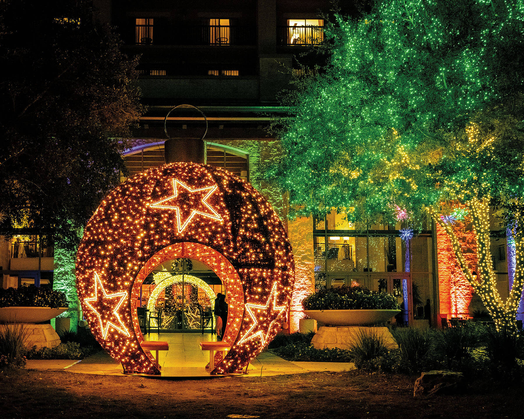 A holiday ornament made of twinkly lights and a star sits in front of a hotel entryway with other light displays