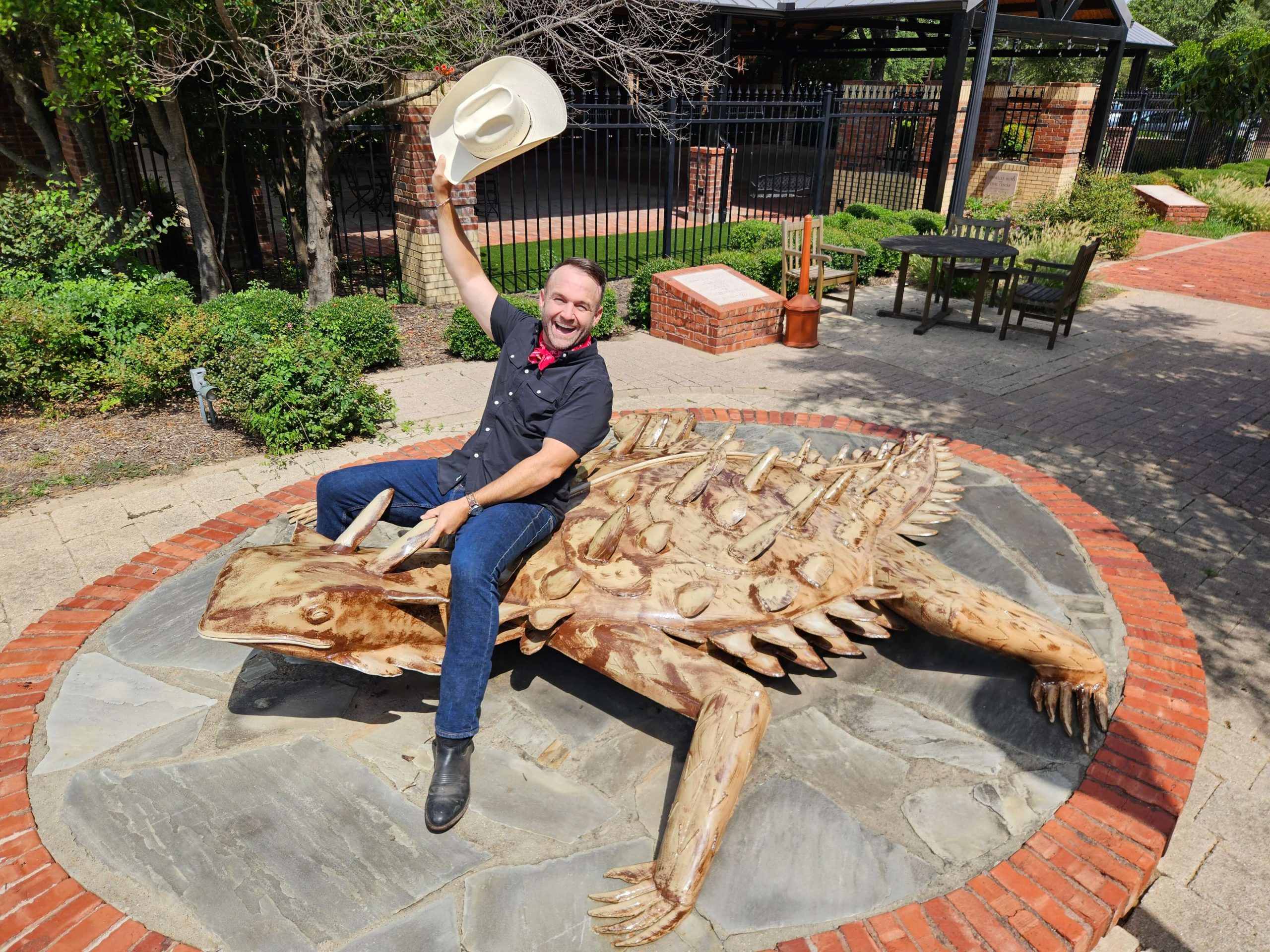 A man rides a statue of a horned lizard.