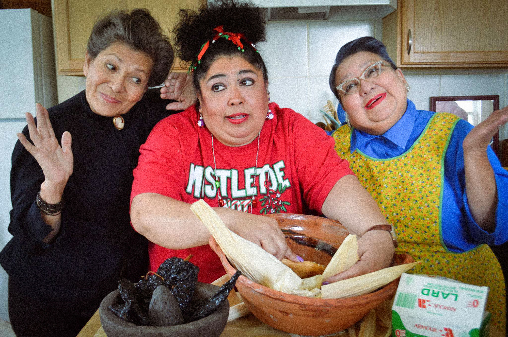 Three women surround a bowl of dough in a kitchen to make tamales