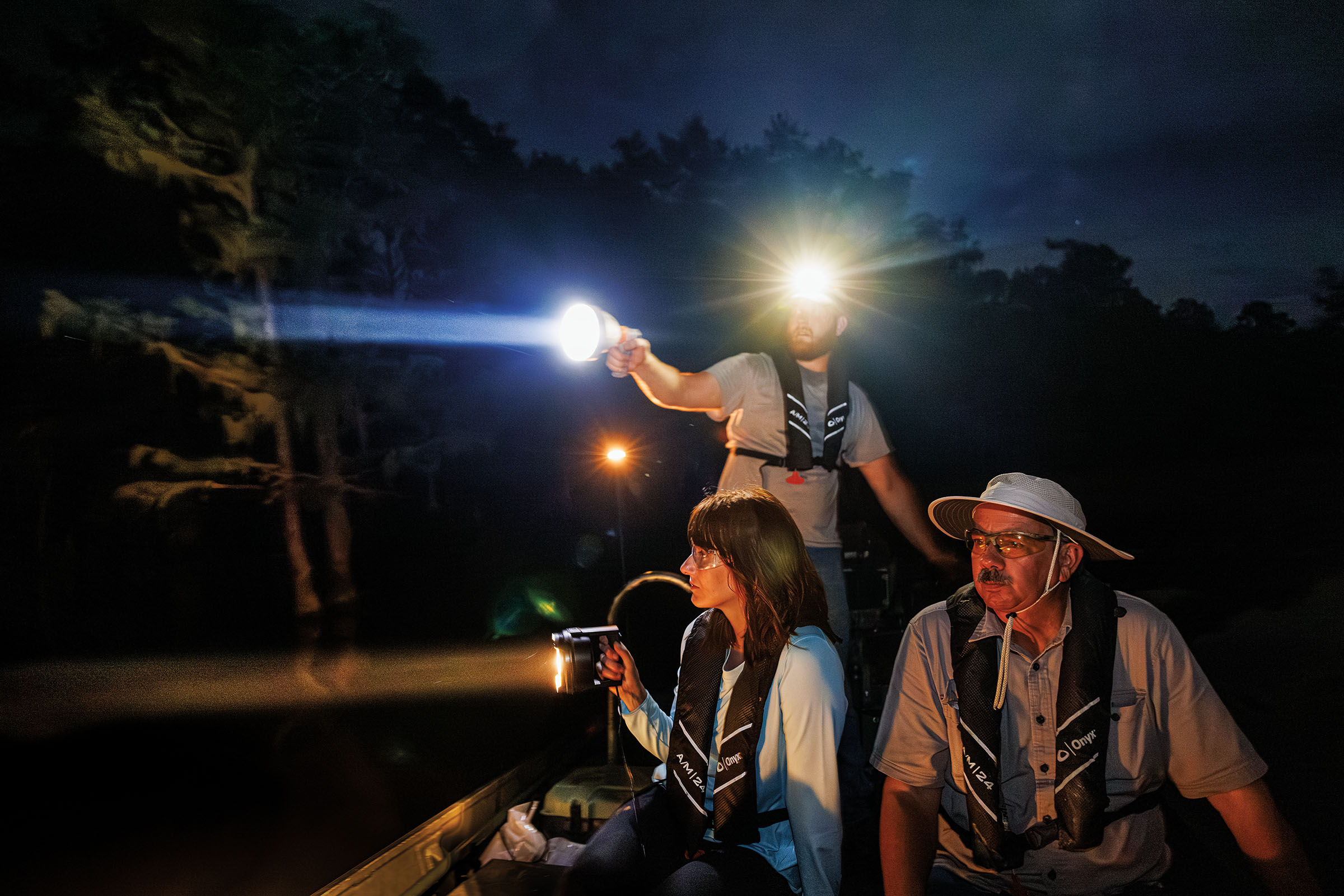 A group of people wearing headlamps shine lights from a boat in darkness