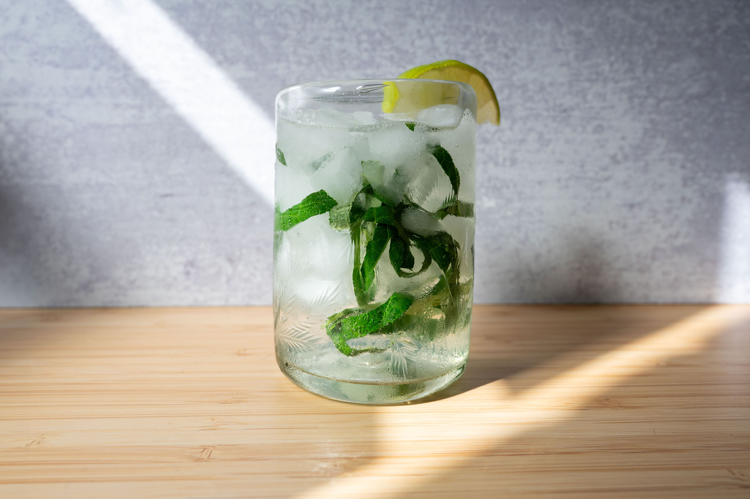 A cocktail with ice in a glass with a green herb inside