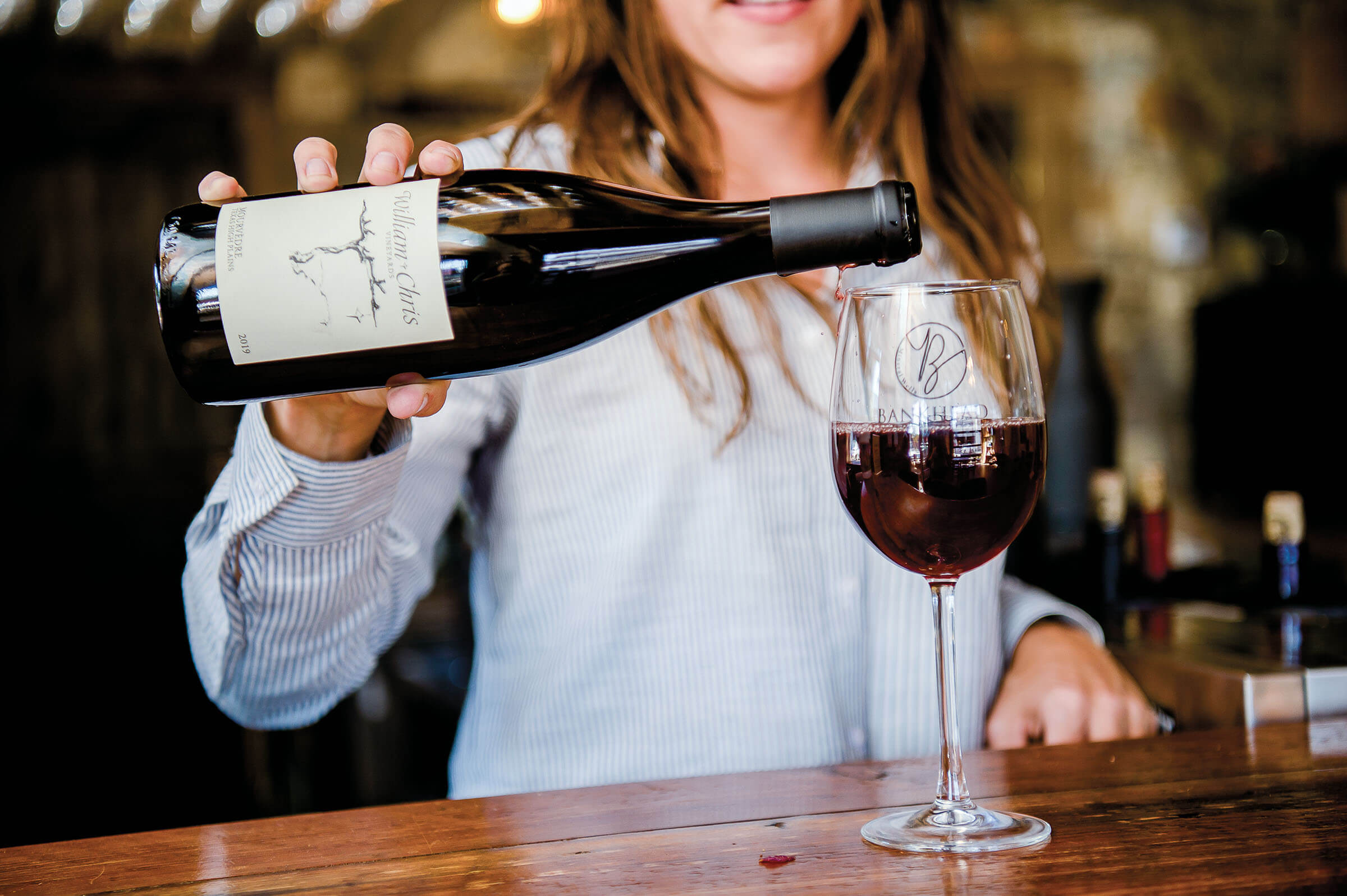A woman pours a bottle of red wine into a glass