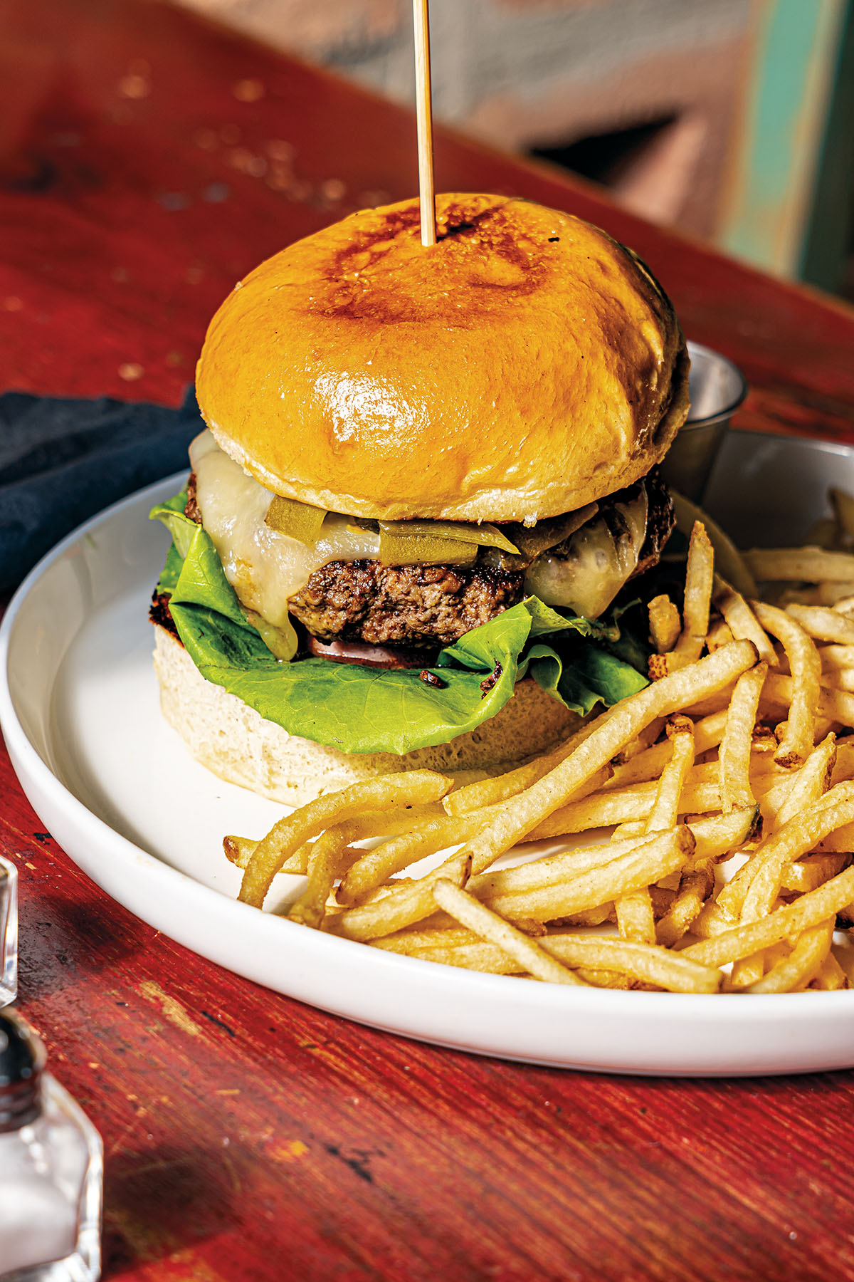 A burger on a golden brioche bun with French fries on a white plate
