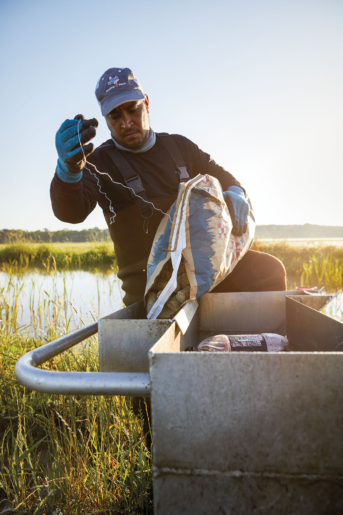 A man in a baseball cap holds a large bag and piece of string in a boat in a swampy area