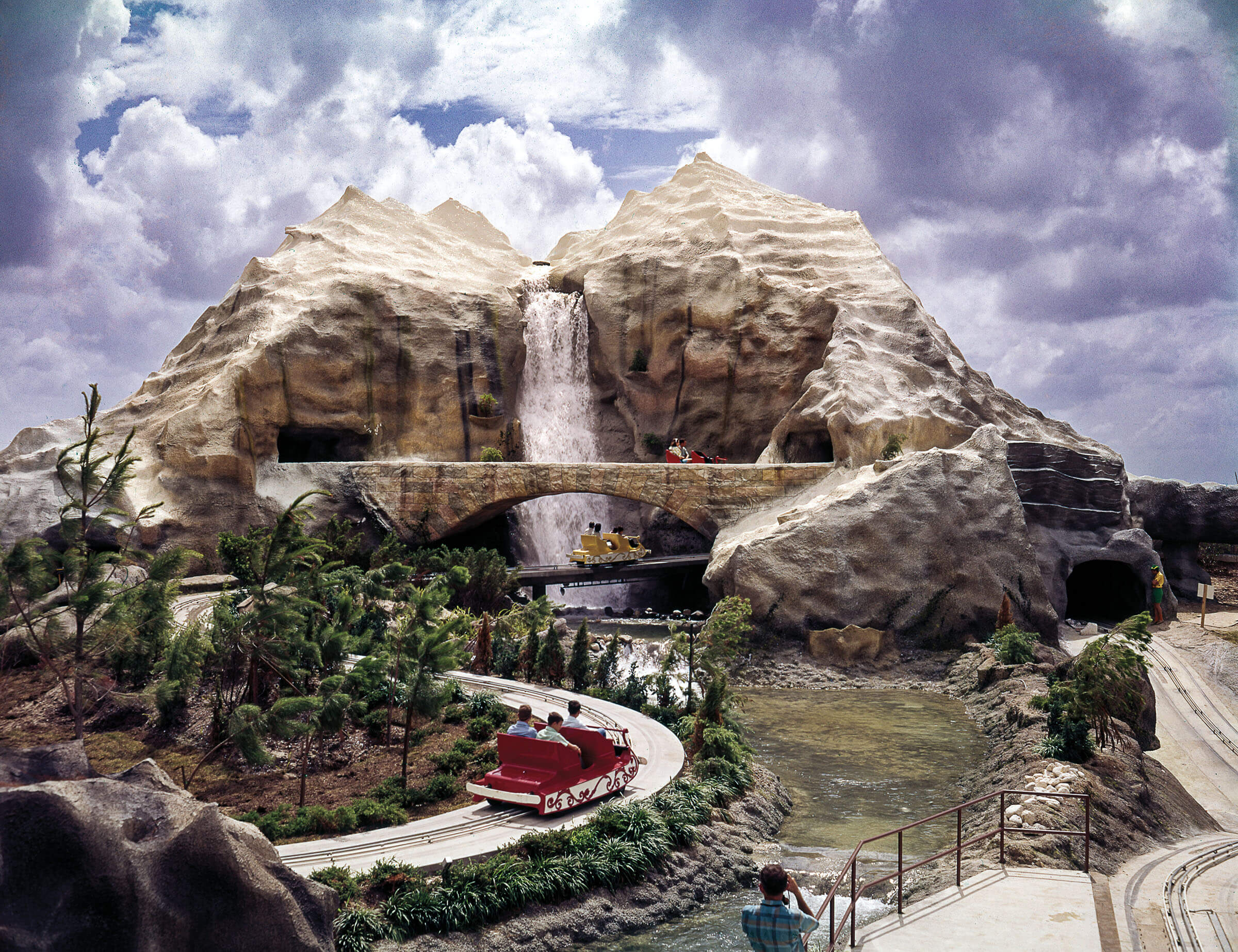An amusement park ride moves toward an artificial snow-capped mountain peak
