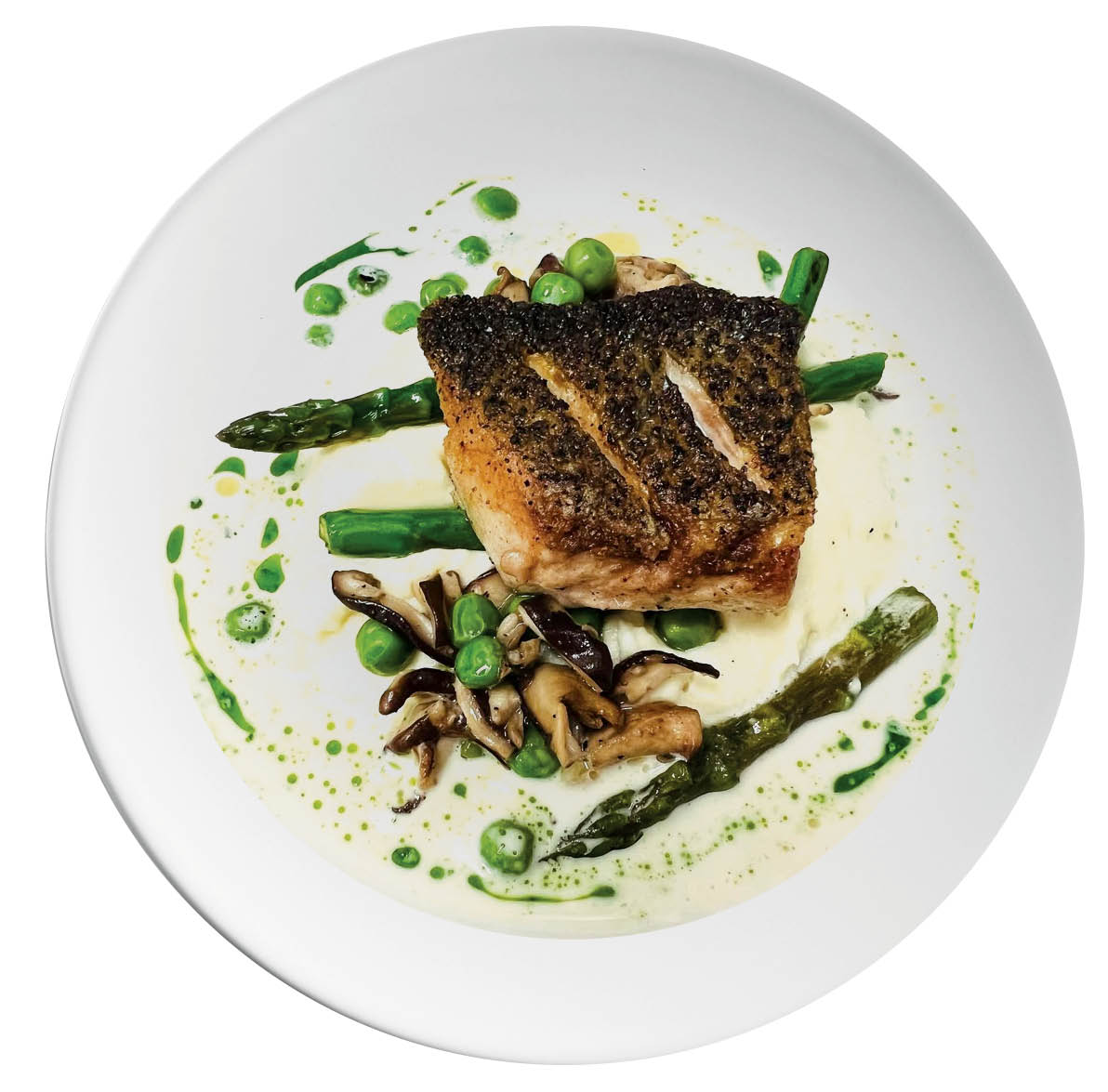 A piece of fish and vegetables in a cream-colored sauce on a white plate