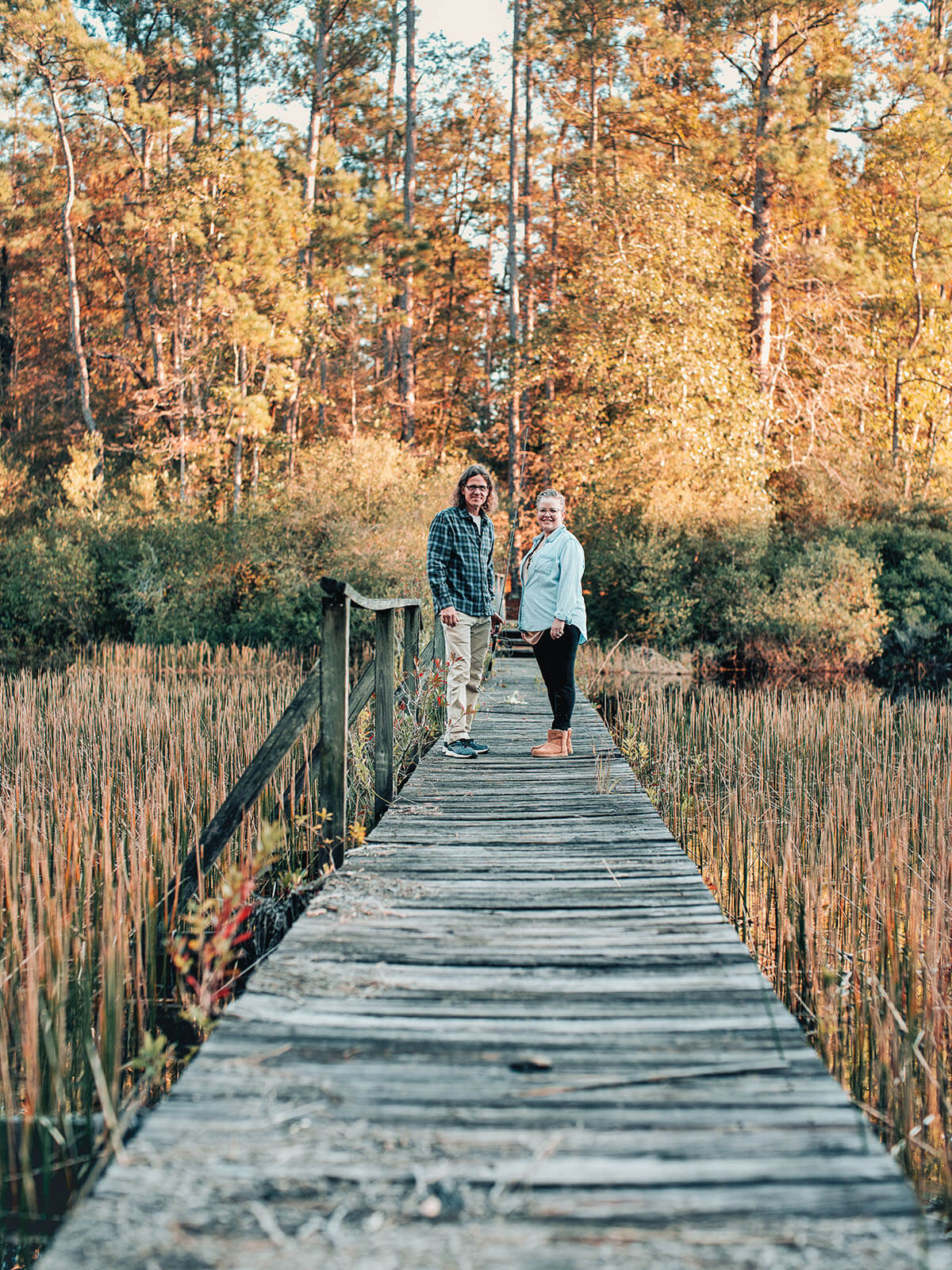 Two people stand at the end of a long wooden boardwalk