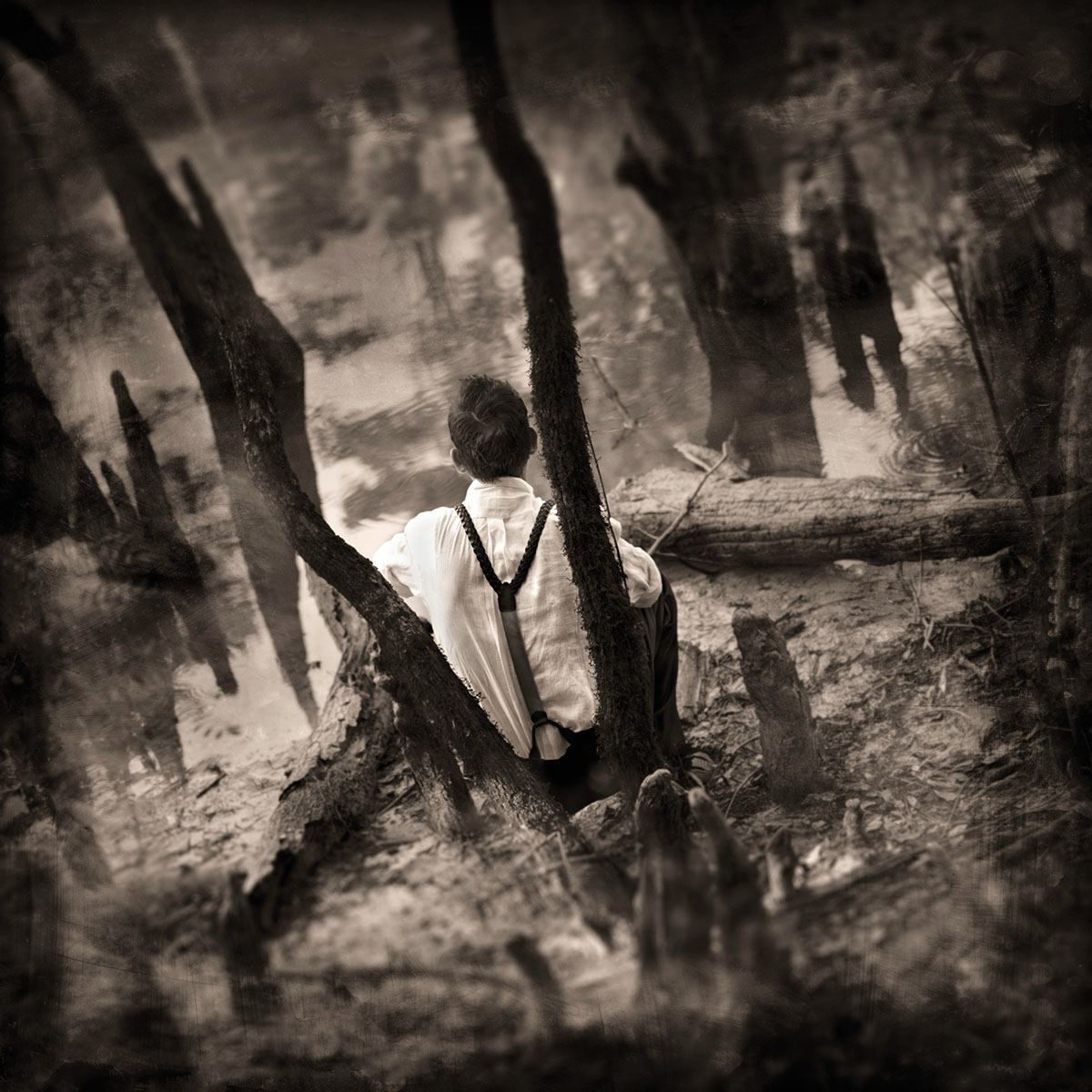 A sepia-toned image of a person sitting on a bank under tall trees