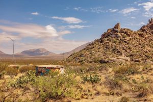 A concrete tank covered in graffiti sits in a desert setting under a rocky mountain