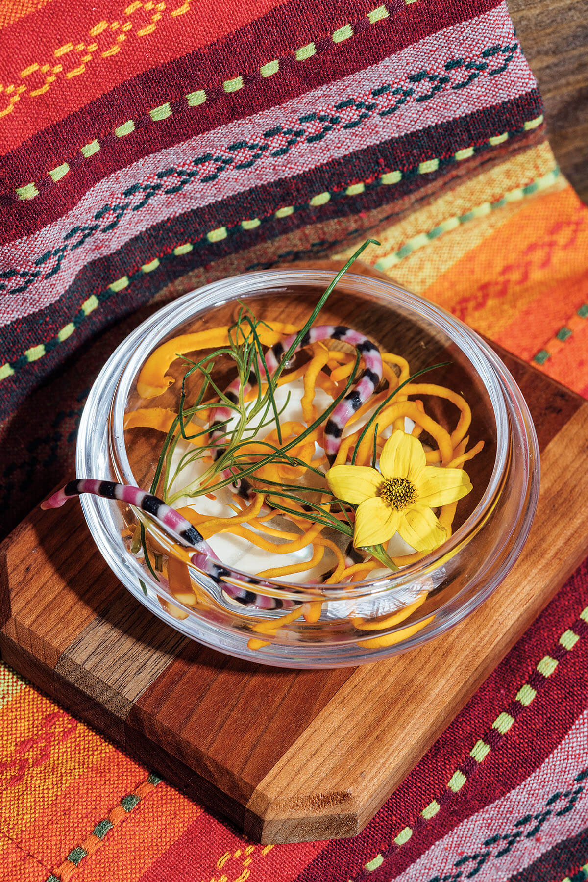 An overhead view of a brightly-colored noodle dish with a flower on a brightly-patterned background