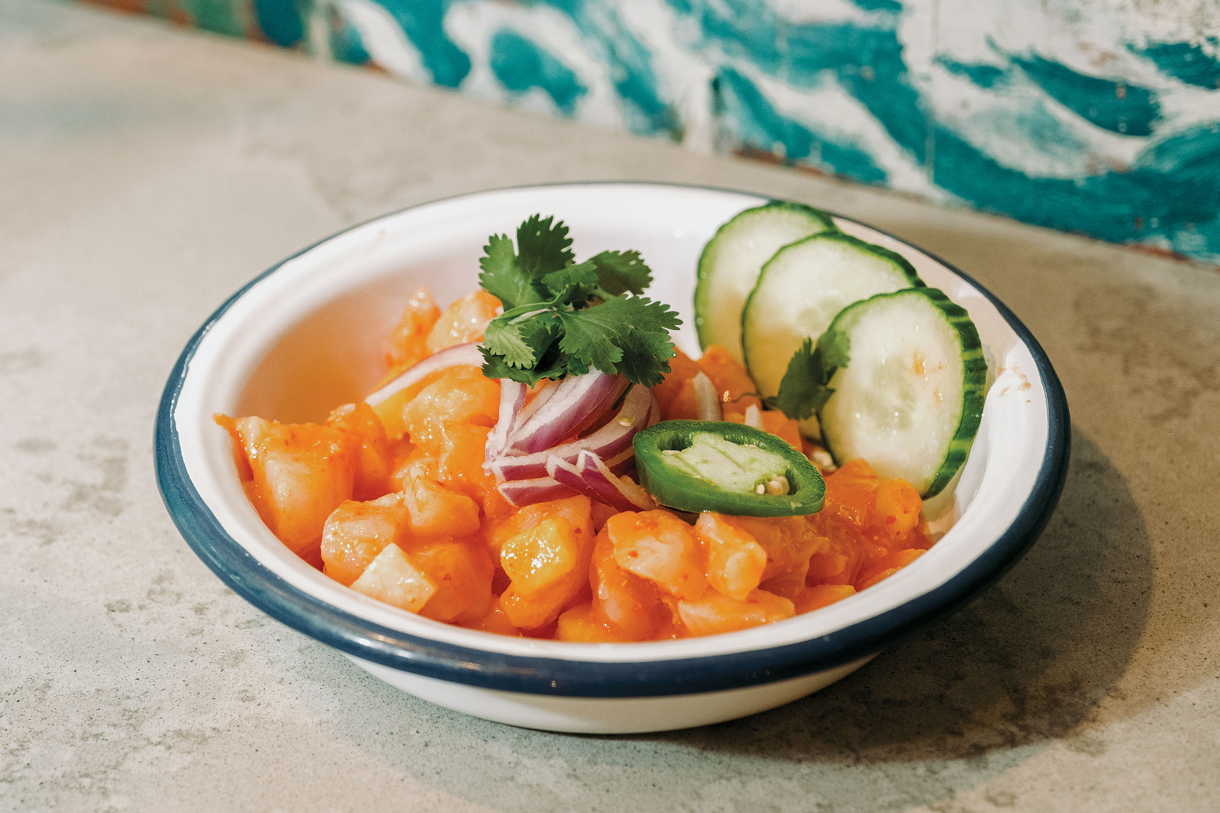 Bright orange fish with green cucumber served in a white ceramic bowl