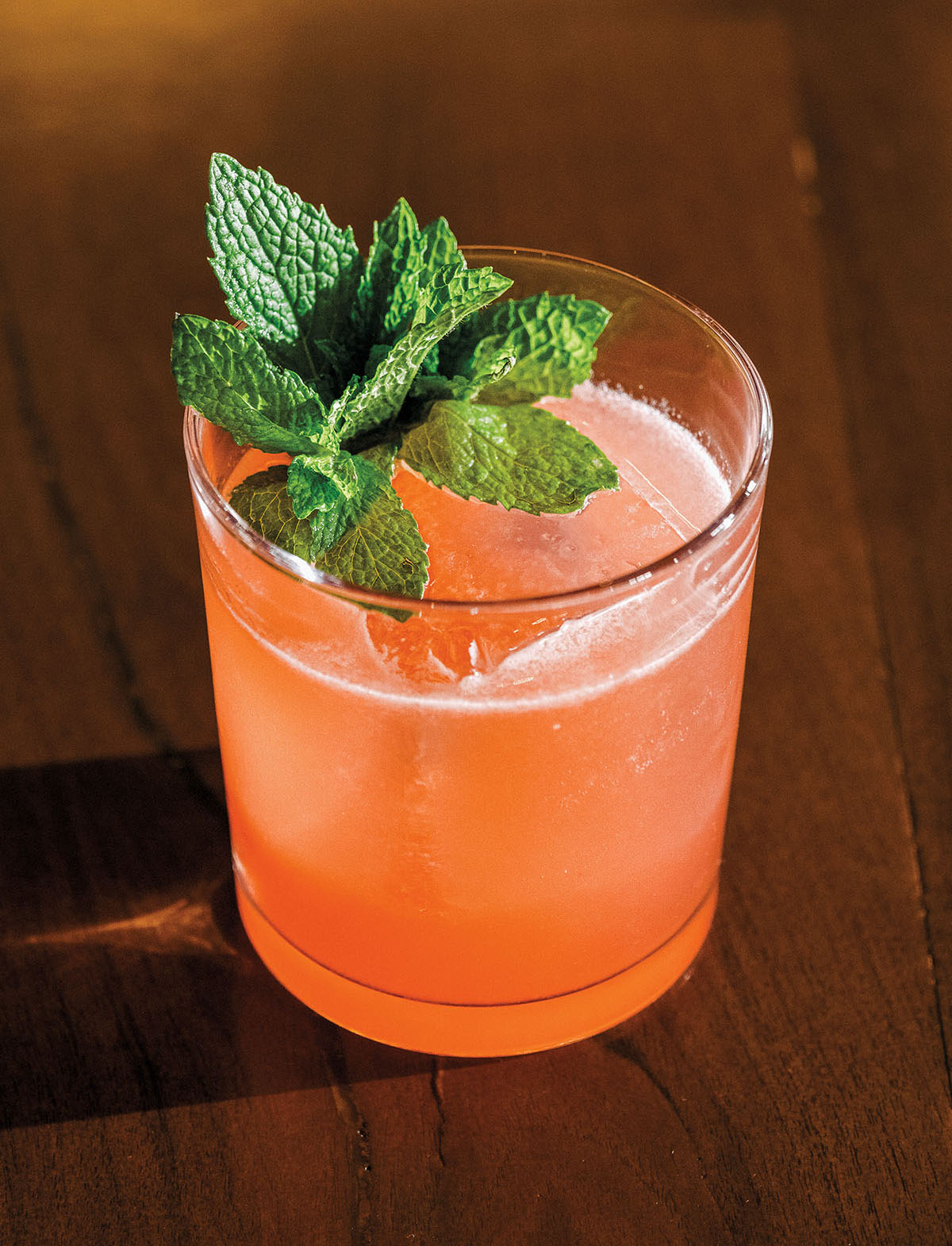 A pink-orange cocktail in a small glass cup with ice and a mint garnish