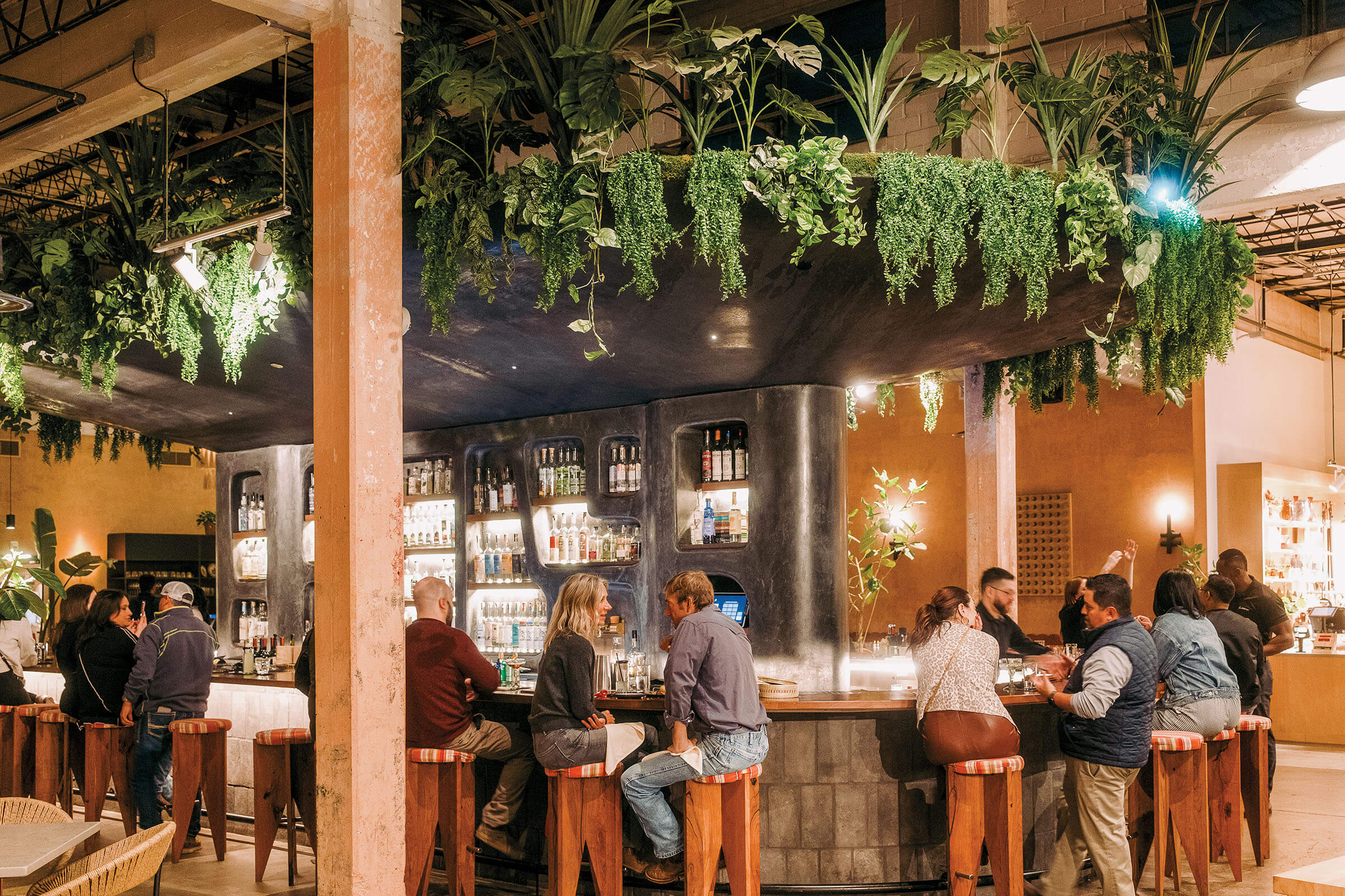 A group of people sit at a wooden bar under greenery
