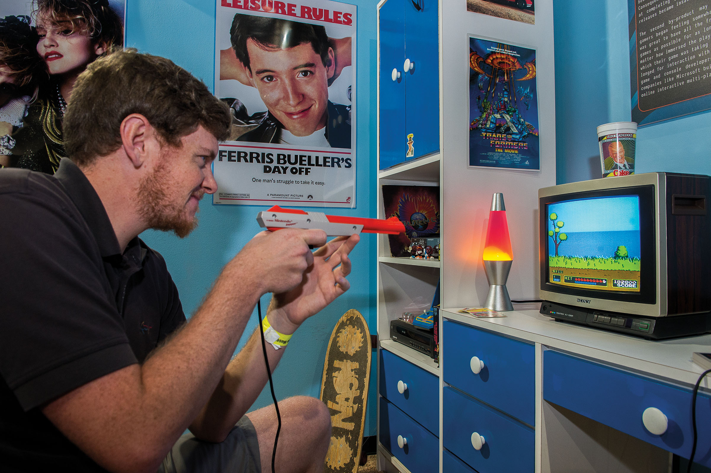 A person uses a plastic gun to play a video game in a blue room