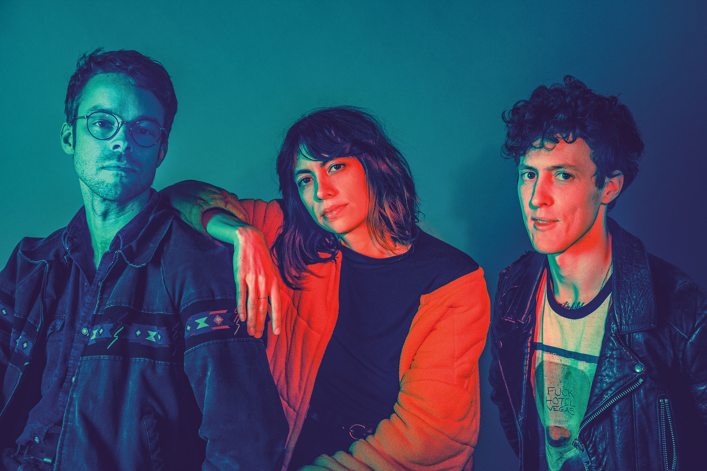 An artistically-lighted portrait of three people in front of a dark blue wall