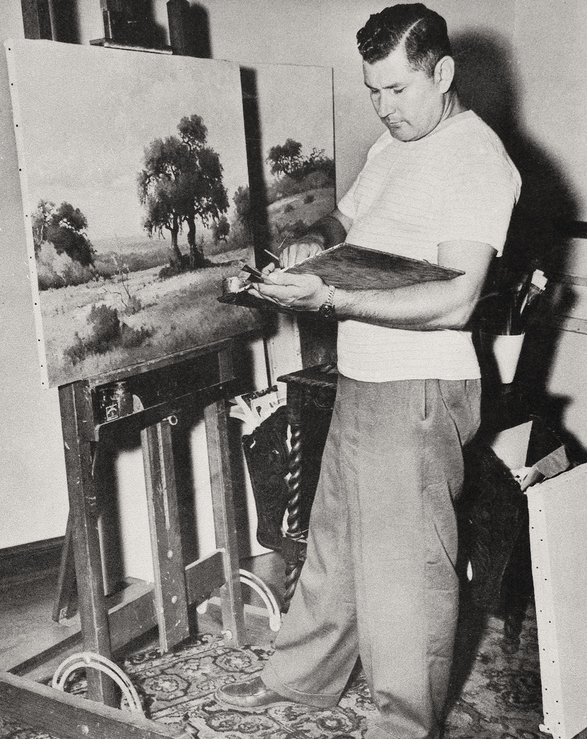 A black and white photo of a painter standing with an easel and brush