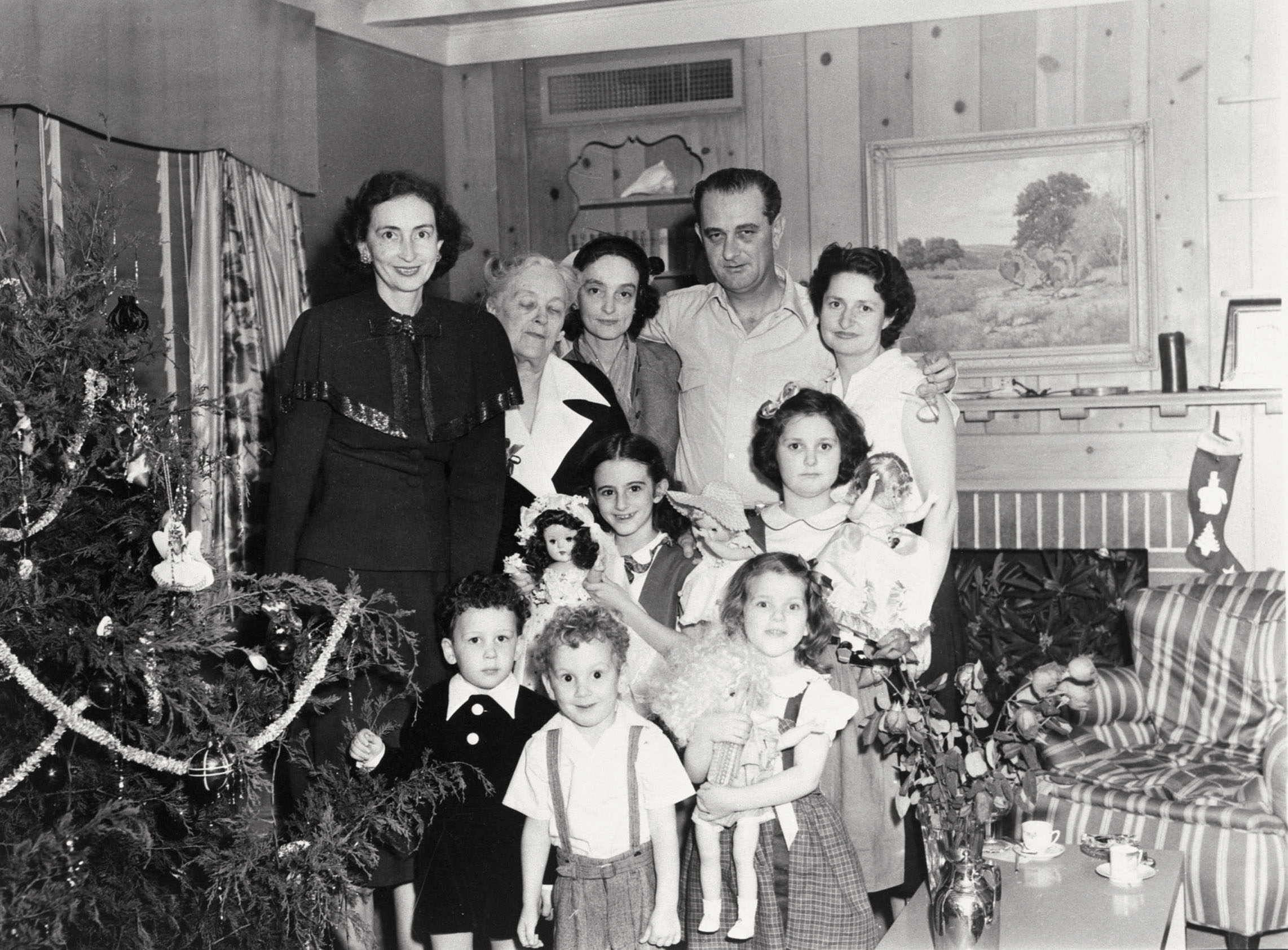 A black and white photo of a group of people posed in front of a landscape painting