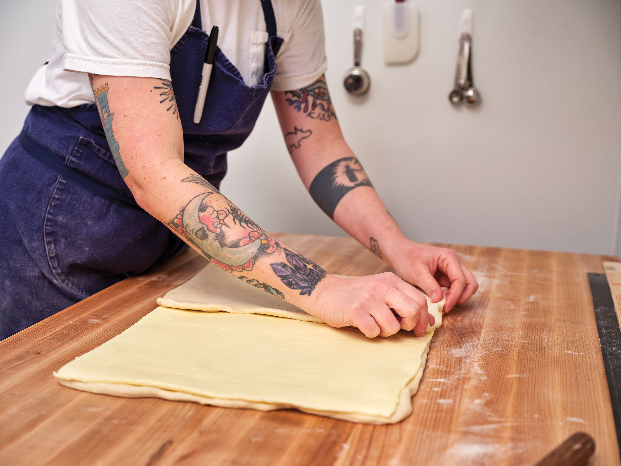 A person with tattoos on their arms works a large sheet of dough